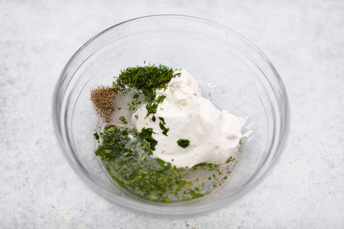 This refreshing German cucumber salad, or Gurkensalat, is easy to throw together and is so flavorful. Thinly sliced cucumbers and fresh herbs are infused in a creamy, tangy sauce. It makes the perfect healthy snack or side dish. Overhead shot of sour cream. dill, parsley, salt, pepper, vinegar and sugar in a mixing bowl.