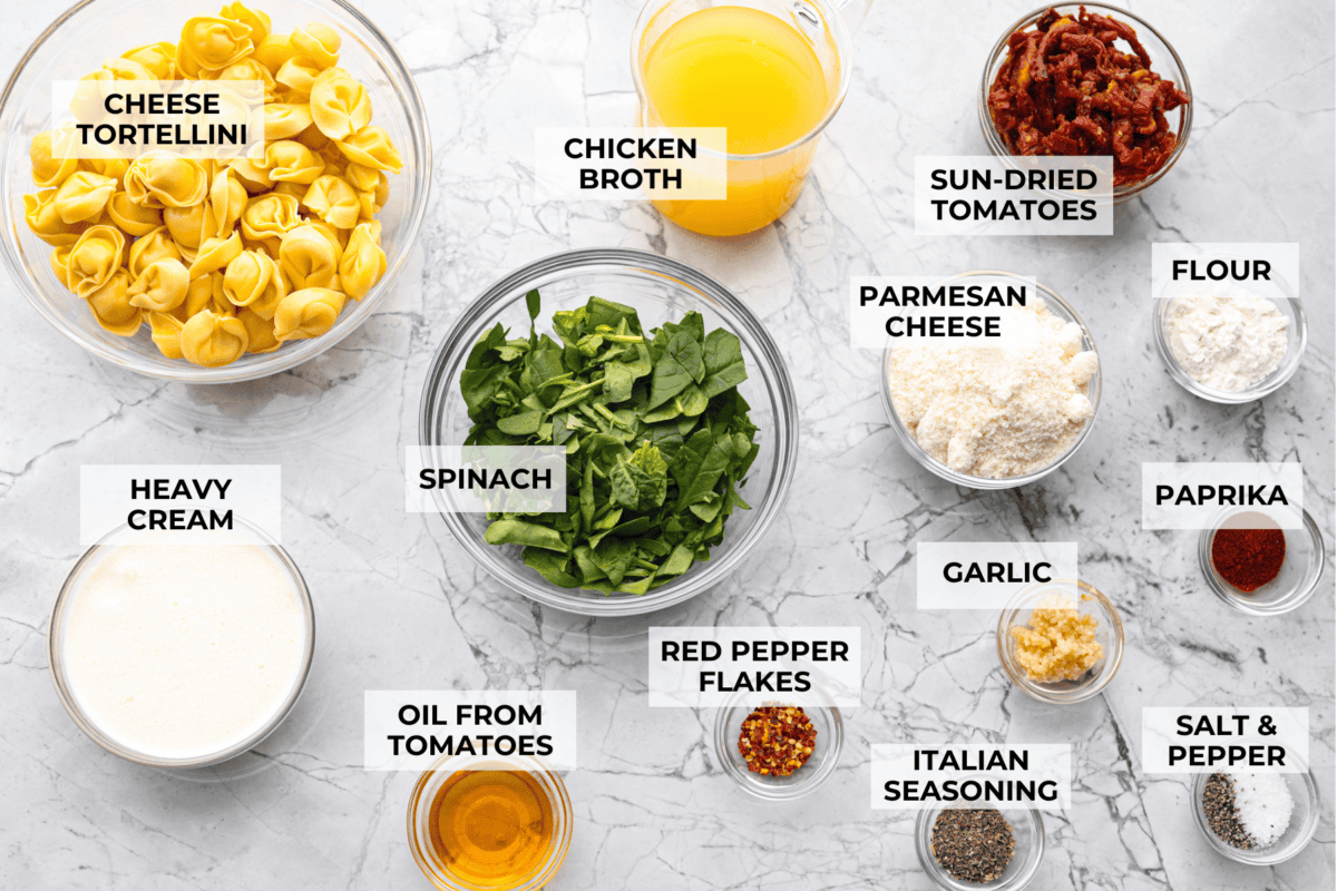 Get ready to impress with One-Pan Marry Me Tortellini! This 20-minute dish is made with cheese tortellini simmered in a rich sun-dried tomato cream sauce infused with garlic, fresh spinach, and parmesan. You'll fall in love with every bite! Overhead shot of labeled ingredients.