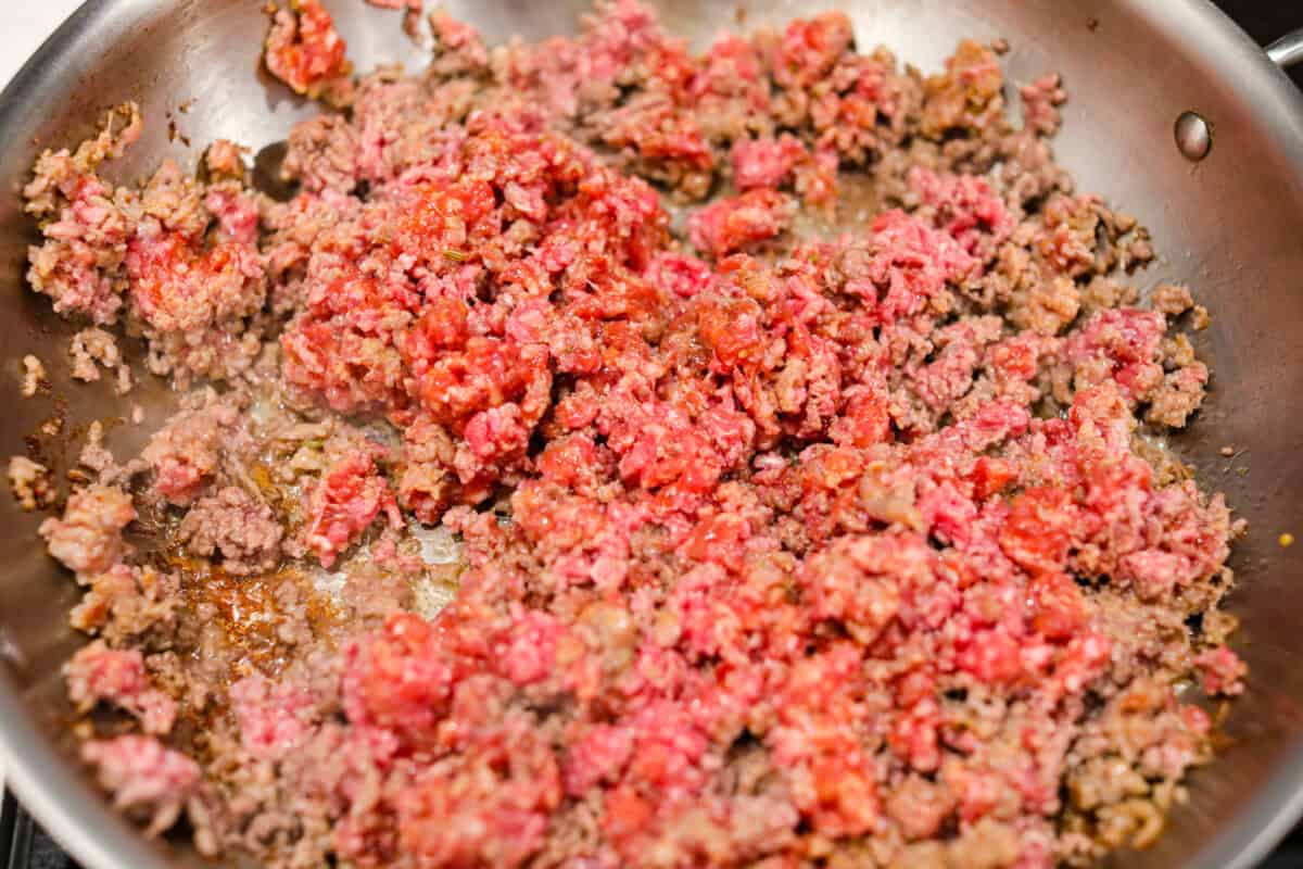 Million Dollar Baked Ziti is the ultimate comfort food that tastes like a million bucks! It's packed with layers of tender noodles, ground meat, spaghetti sauce, and plenty of cheesy goodness. There is something for the whole family in this hearty, crowd-pleasing dish! Overhead shot of ground beef and Italian sausage cooking in a skillet.