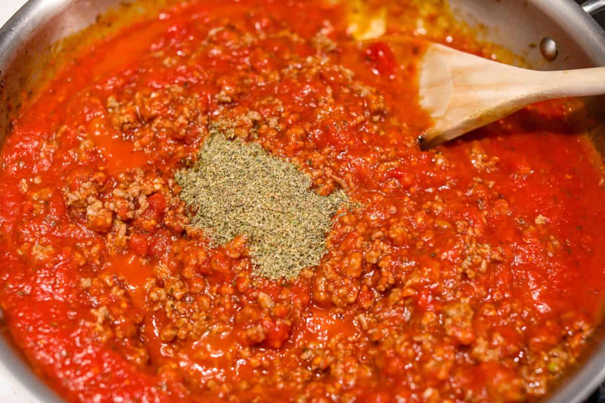 Million Dollar Baked Ziti is the ultimate comfort food that tastes like a million bucks! It's packed with layers of tender noodles, ground meat, spaghetti sauce, and plenty of cheesy goodness. There is something for the whole family in this hearty, crowd-pleasing dish! Overhead shot of cooked meat with spaghetti sauce and Italian seasoning added.