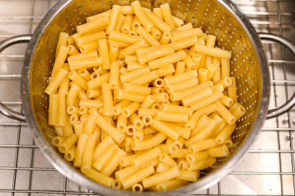 Million Dollar Baked Ziti is the ultimate comfort food that tastes like a million bucks! It's packed with layers of tender noodles, ground meat, spaghetti sauce, and plenty of cheesy goodness. There is something for the whole family in this hearty, crowd-pleasing dish! Overhead shot of cooked ziti noodles in a colander.