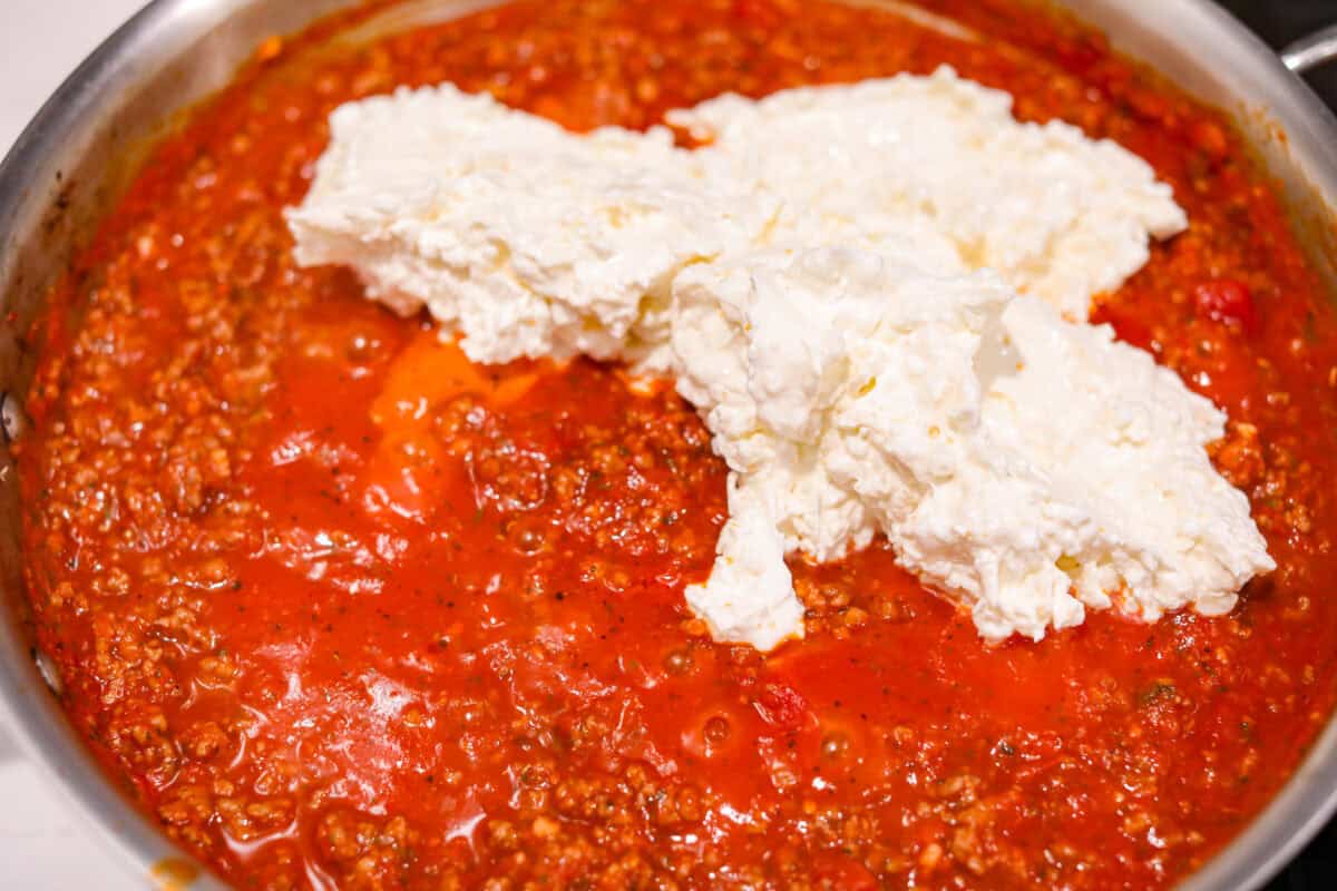 Million Dollar Baked Ziti is the ultimate comfort food that tastes like a million bucks! It's packed with layers of tender noodles, ground meat, spaghetti sauce, and plenty of cheesy goodness. There is something for the whole family in this hearty, crowd-pleasing dish! Overhead shot of meat sauce with the cheese mixture on top.