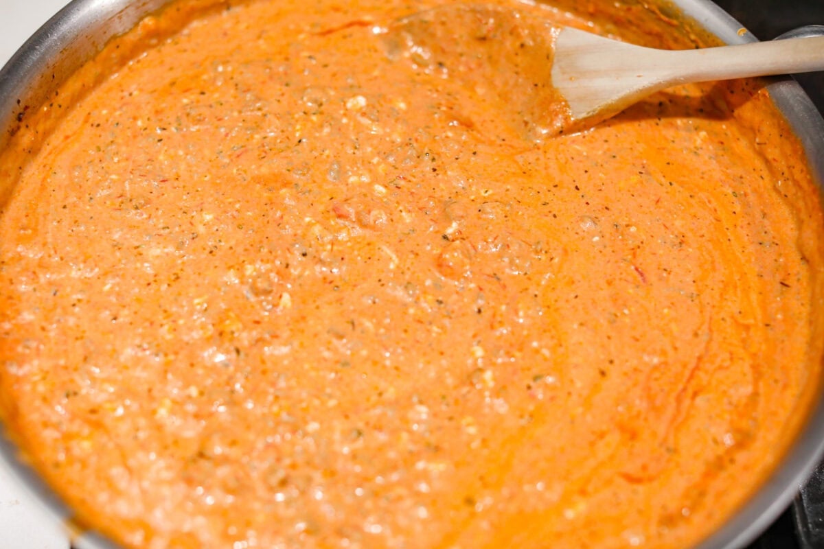 Million Dollar Baked Ziti is the ultimate comfort food that tastes like a million bucks! It's packed with layers of tender noodles, ground meat, spaghetti sauce, and plenty of cheesy goodness. There is something for the whole family in this hearty, crowd-pleasing dish! Overhead shot of the million dollar baked ziti sauce mixed togethe rin a skillet.
