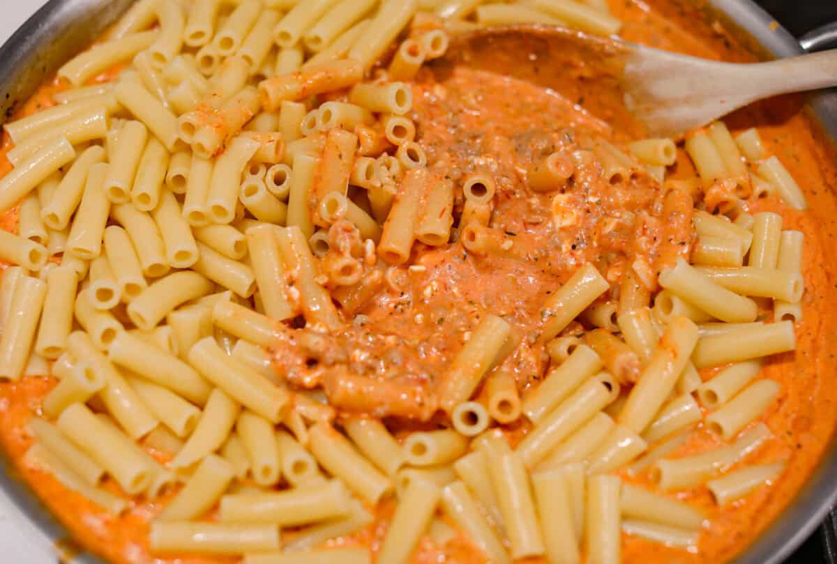 Million Dollar Baked Ziti is the ultimate comfort food that tastes like a million bucks! It's packed with layers of tender noodles, ground meat, spaghetti sauce, and plenty of cheesy goodness. There is something for the whole family in this hearty, crowd-pleasing dish! Overhead shot of ziti noodles being mixed in with the sauce.