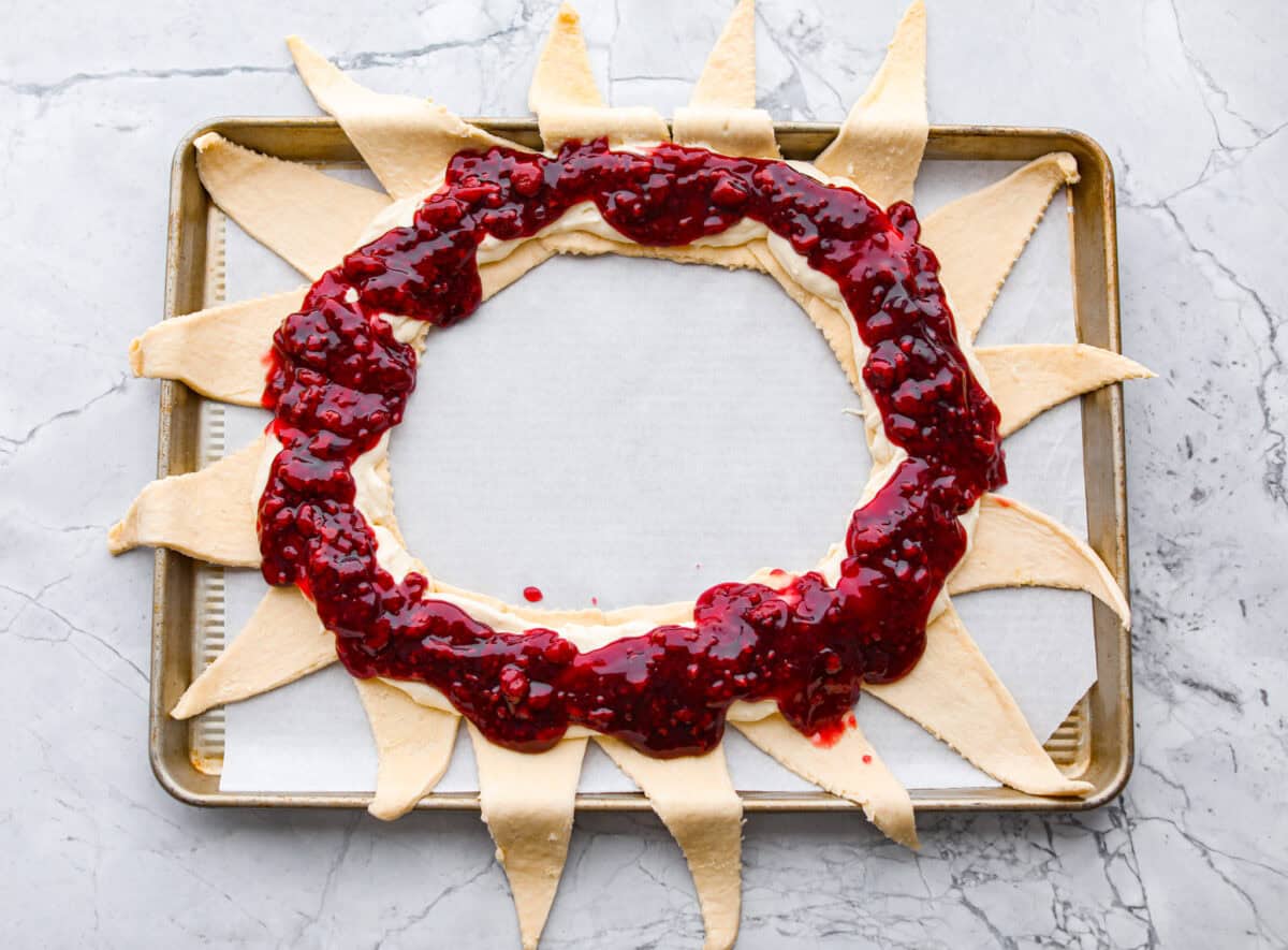 This Raspberry Cream Cheese Crescent Ring is a simple pastry with a flaky, golden crust, a sweet and tangy cream cheese filling, and a burst of raspberry flavor. Perfect for breakfast, brunch, or dessert, it's easy to make yet impressively delicious! Overhead shot of the raspberry filling spread over the cream cheese and crescent rolls.