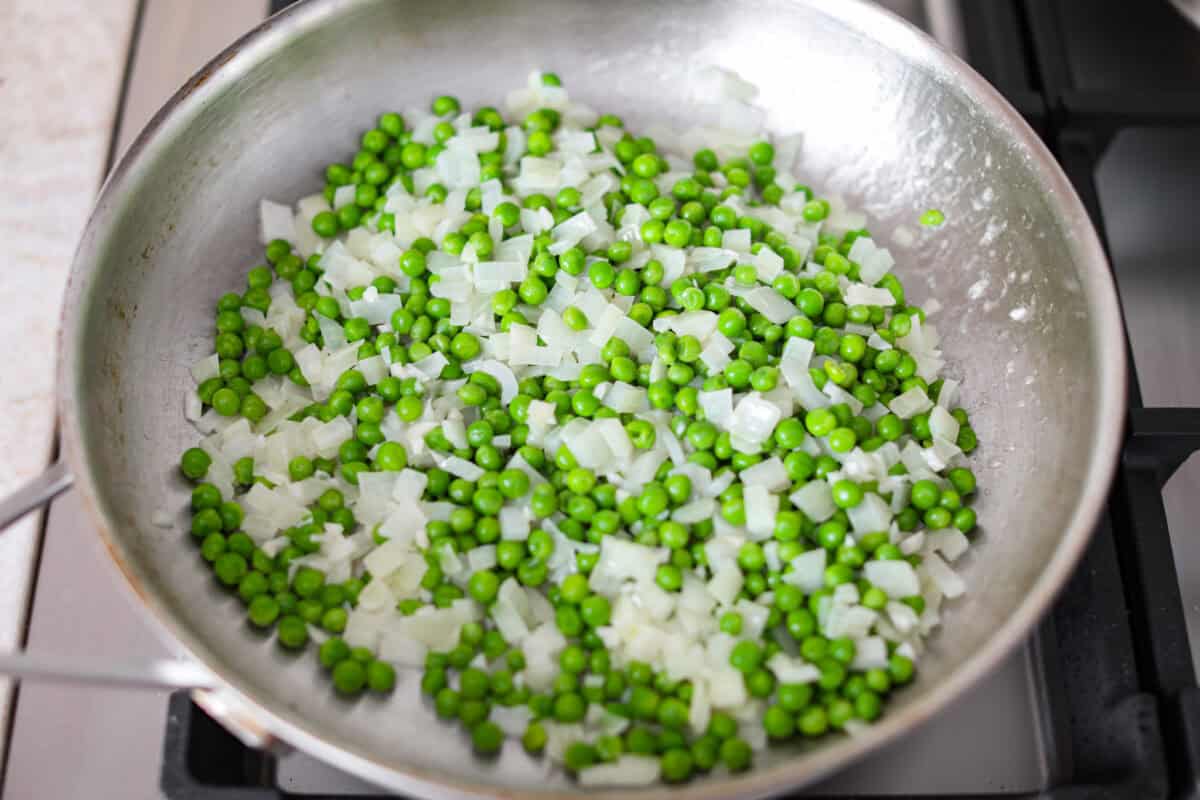 Stanley Tucci pasta casserole is everything you want in a casserole. It's simple to make and incredibly flavorful! TikTok is going crazy over the crispy bacon, tender peas, and the creamy, cheesy sauce that holds everything together! Overhead shot of garlic, onion, and peas sautéing in a pan.