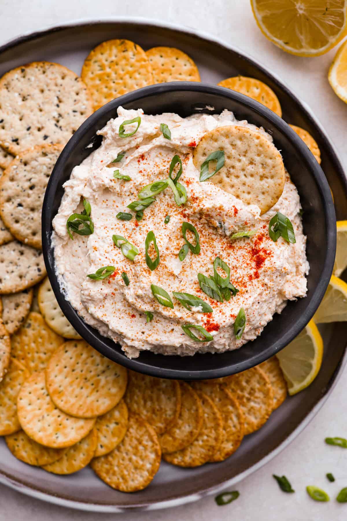 Spice up your appetizer game with Cajun Crab Dip! Packed with tender crab meat, bold Cajun seasoning, and a luscious, creamy base. This dip is irresistibly rich and full of flavor. Serve this at your next gathering with your favorite crispy crackers! Overhead shot of cajun crab dip in a bowl on a serving platter full of crackers.