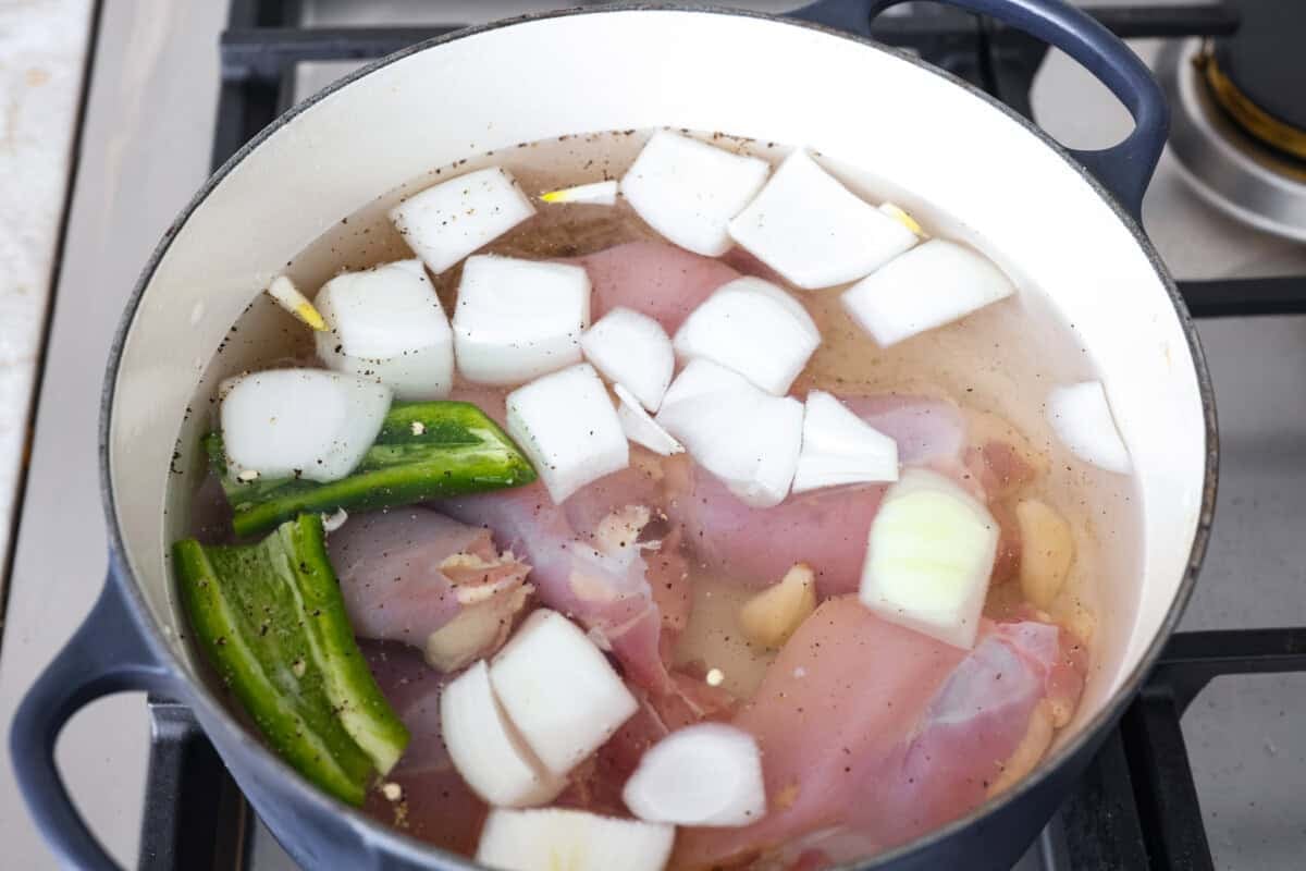 Caldo de Pollo is a comforting and flavorful Mexican chicken soup made with tender chicken, hearty vegetables, and a rich, savory broth. Itโs warm, nourishing, and perfect for cozying up on a chilly day! Overhead shot of a large pot with the water, chicken, onions, jalapeno, garlic, salt and pepper added.