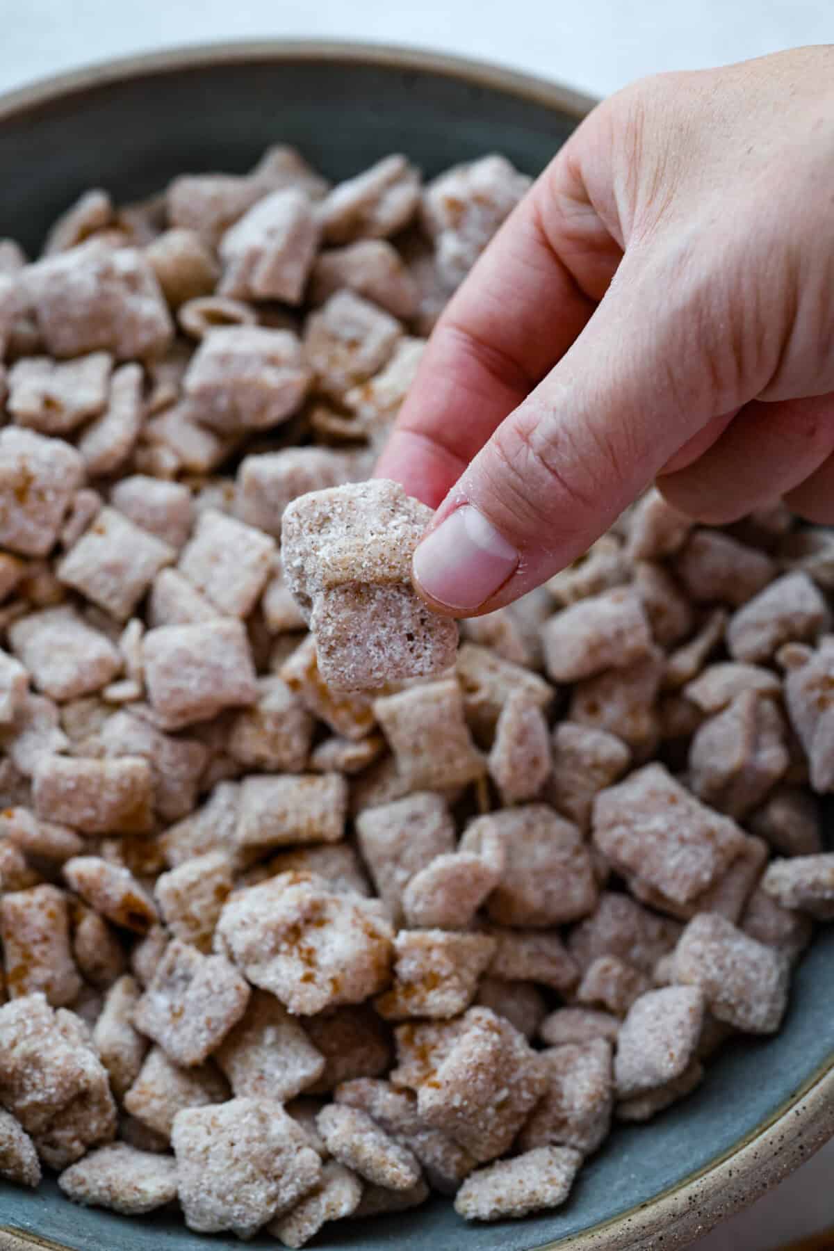 Churro Chex Mix is a fun variation of the popular muddy buddy mix. Sweet cinnamon and sugar mixed with silky white chocolate coat the crunchy cereal to create an addicting treat. It's the perfect snack to whip up for game day, road trips, or weeknights when that sweet tooth hits! Close up shot of someone picking up a chunk of the churro Chex mix.