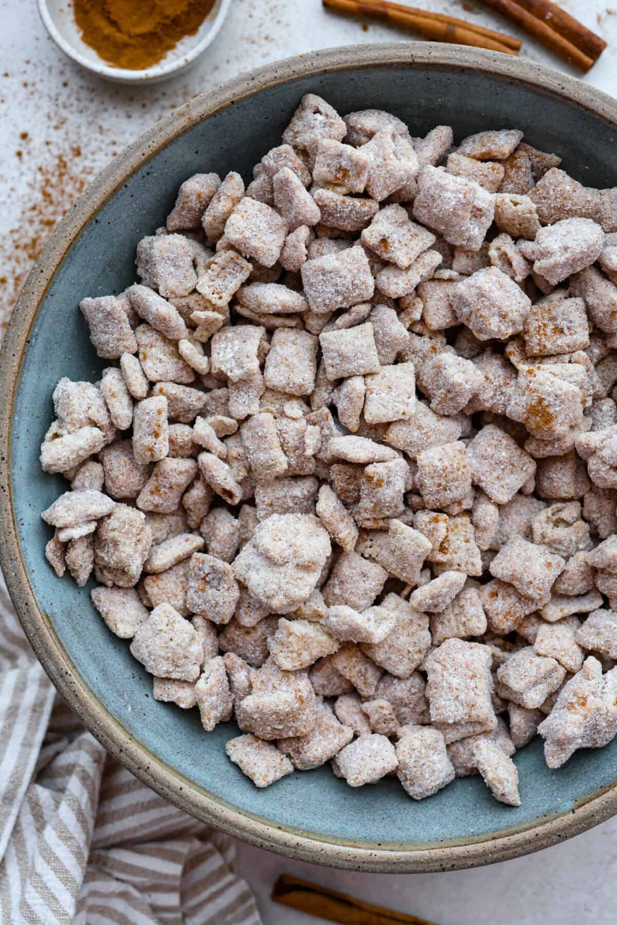 Churro Chex Mix is a fun variation of the popular muddy buddy mix. Sweet cinnamon and sugar mixed with silky white chocolate coat the crunchy cereal to create an addicting treat. It's the perfect snack to whip up for game day, road trips, or weeknights when that sweet tooth hits! Overhead shot of a large bowl of churro Chex mix.