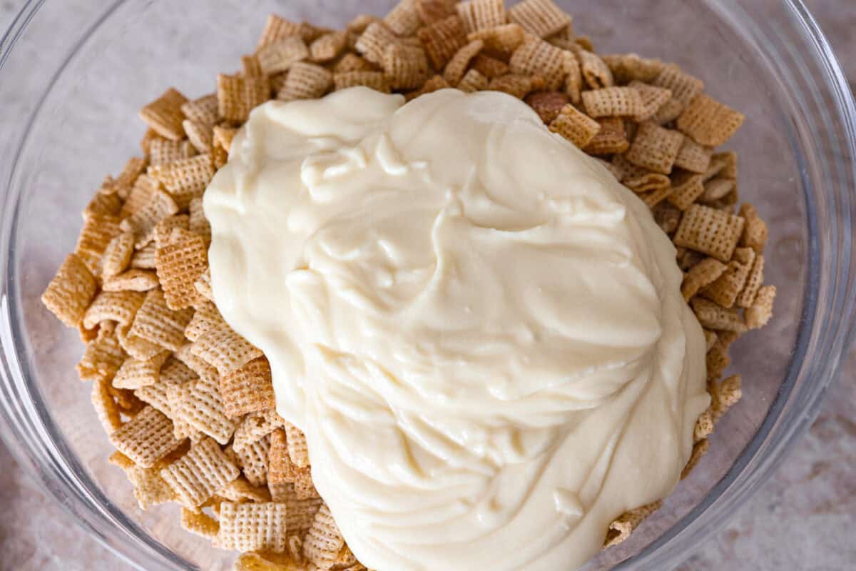 Churro Chex Mix is a fun variation of the popular muddy buddy mix. Sweet cinnamon and sugar mixed with silky white chocolate coat the crunchy cereal to create an addicting treat. It's the perfect snack to whip up for game day, road trips, or weeknights when that sweet tooth hits! Overhead shot of the melted white chocolate and butter mixture poured over the cereal.