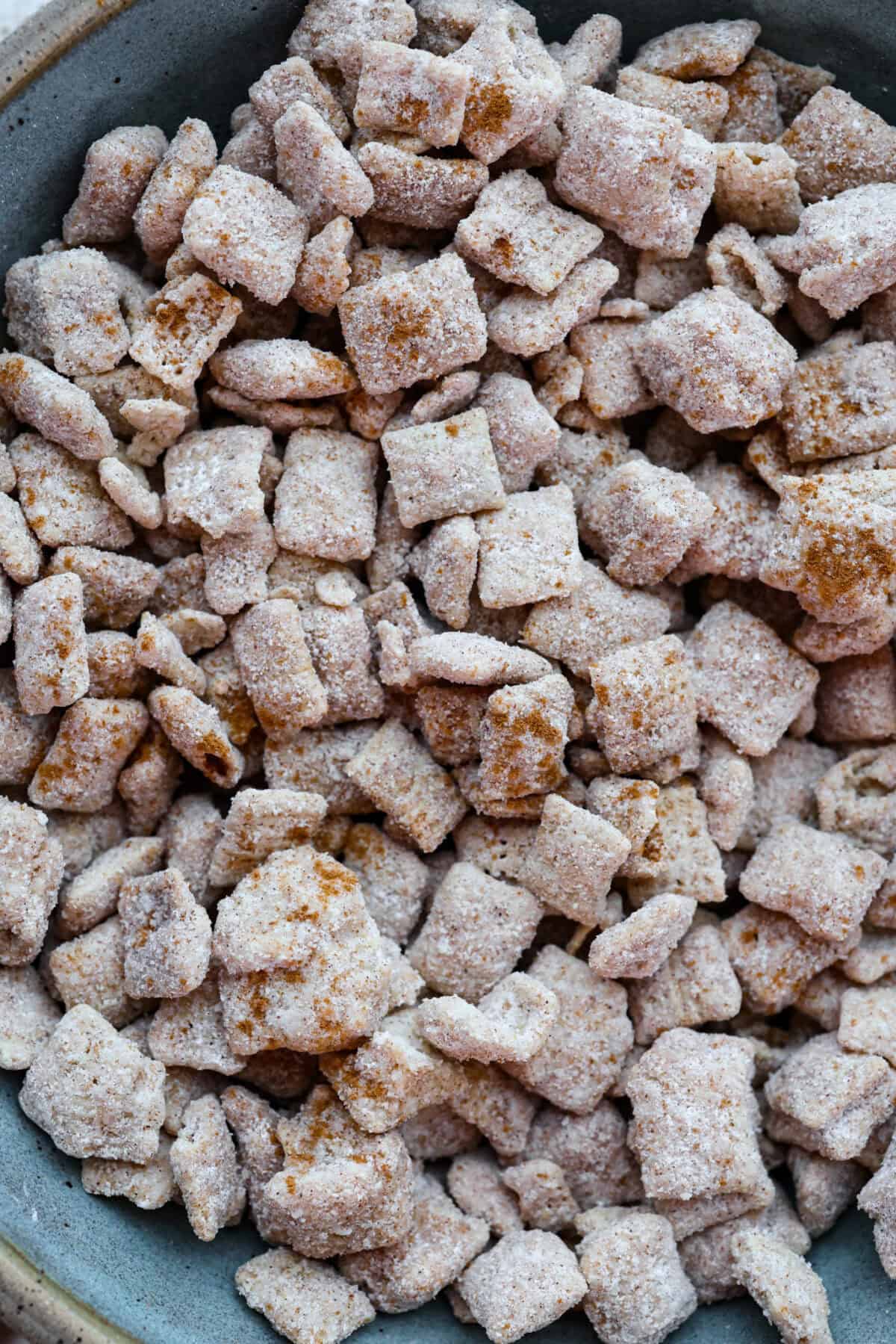 Churro Chex Mix is a fun variation of the popular muddy buddy mix. Sweet cinnamon and sugar mixed with silky white chocolate coat the crunchy cereal to create an addicting treat. It's the perfect snack to whip up for game day, road trips, or weeknights when that sweet tooth hits! Close up shot of churro Chex mix.