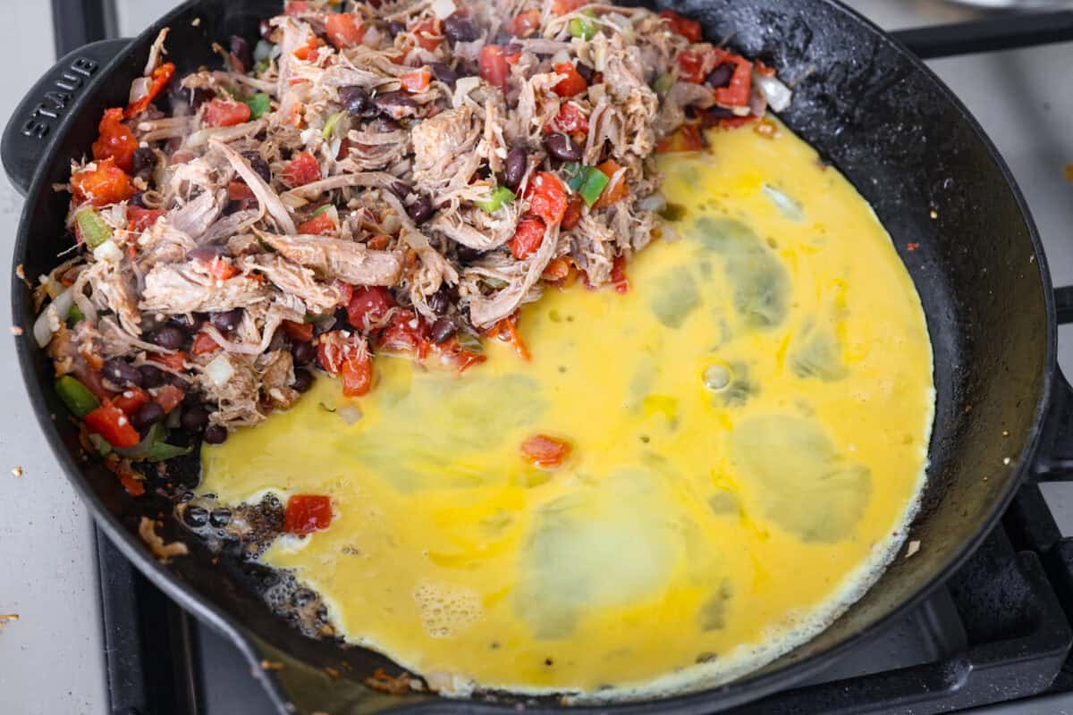 Cowboy Fried Rice is a Tex-Mex twist on the classic! It's loaded with bold spices and hearty ingredients like pulled pork, black beans, and diced tomatoes. Made in one skillet and ready in just 30 minutes, itโs the perfect quick and satisfying meal for busy nights. Overhead shot of pork mixture pushed to the side in a skillet with eggs cooking next to it.