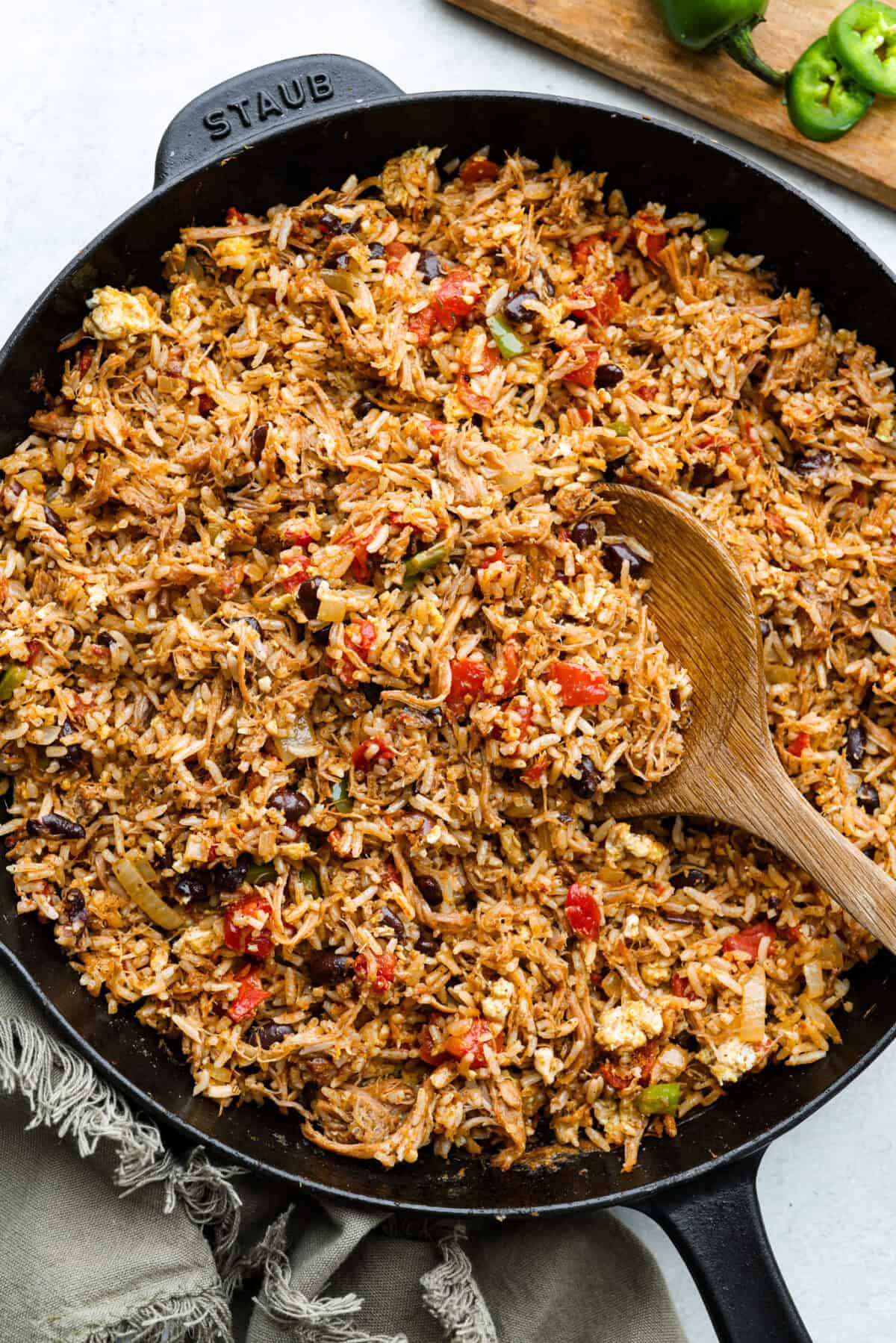 Cowboy Fried Rice is a Tex-Mex twist on the classic! It's loaded with bold spices and hearty ingredients like pulled pork, black beans, and diced tomatoes. Made in one skillet and ready in just 30 minutes, itโs the perfect quick and satisfying meal for busy nights. Overhead shot of cowboy fried rice in a skillet with wooden spoon.