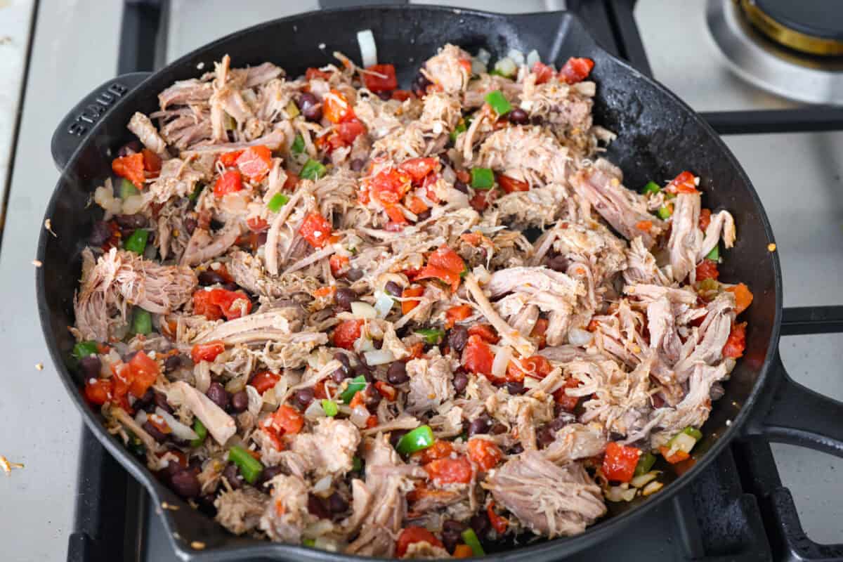 Cowboy Fried Rice is a Tex-Mex twist on the classic! It's loaded with bold spices and hearty ingredients like pulled pork, black beans, and diced tomatoes. Made in one skillet and ready in just 30 minutes, itโs the perfect quick and satisfying meal for busy nights. Overhead shot of pork, beans, and diced tomatoes added in to the cooked vegetables.