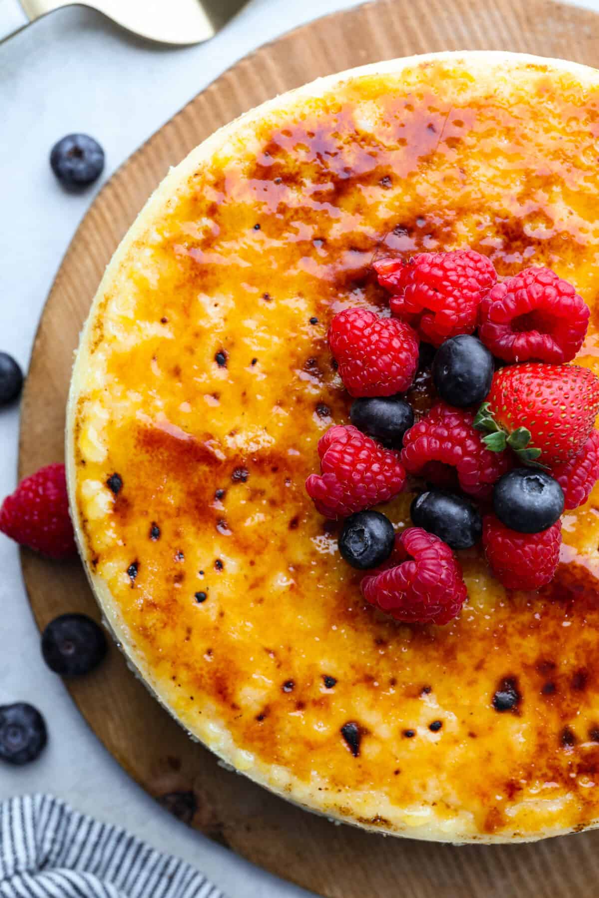 Creme Brulee Cheesecake is the perfect merging of two beloved desserts! It has the rich, creamy texture of cheesecake with the caramelized sugar topping of classic crรจme brรปlรฉe. This irresistible treat is the best of both worlds! Overhead shot of creme brรปlรฉe cheesecake with berries on top.