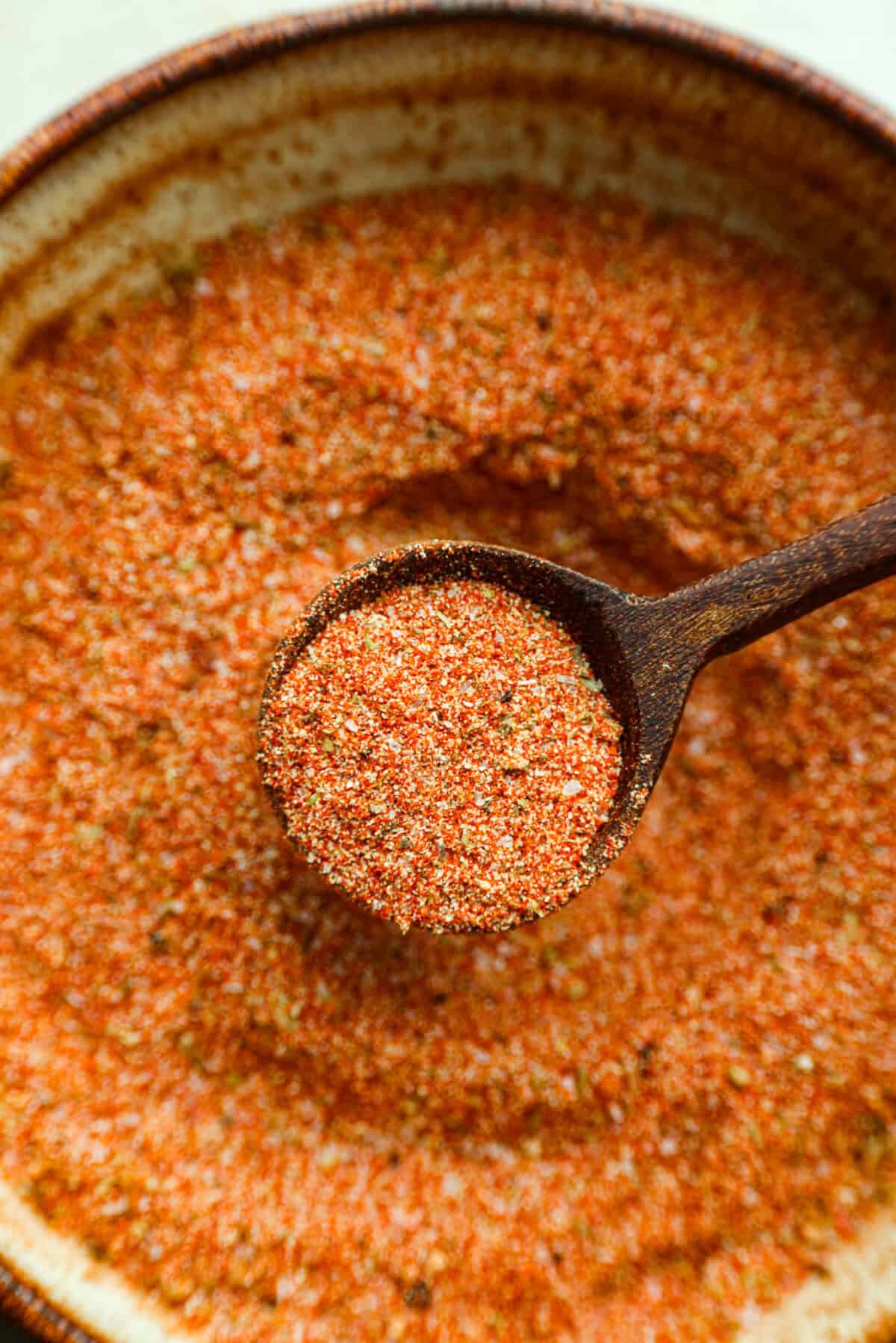 Creole seasoning is a bold and flavorful spice blend that brings the lively taste of Louisiana to your kitchen! It has the perfect balance of herbs, spices, and a touch of heat. It adds depth to everything from gumbo and jambalaya to roasted veggies and seafood. Close up shot of a scoop of creole seasoning in a small wooden spoon.