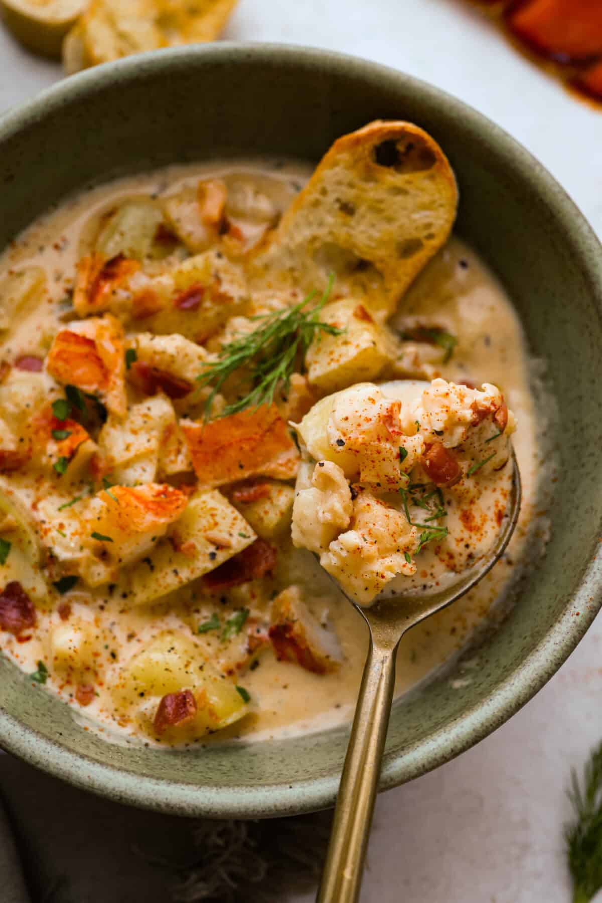 Creamy, indulgent Lobster Chowder takes only 40 minutes to make and is incredibly flavorful! Tender potatoes, crisp bacon, and luscious lobster are enveloped in a creamy, velvety broth. It would be a great soup to serve on Valentine's Day or a special occasion, but easy enough for any night of the week. Overhead shot of a spoon with a bite of lobster chowder being held over a bowl of chowder.