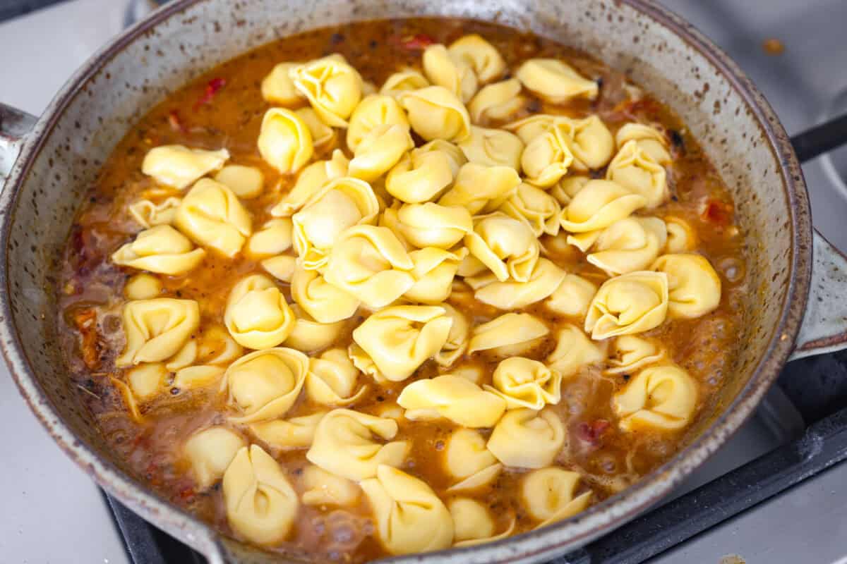 Get ready to impress with One-Pan Marry Me Tortellini! This 20-minute dish is made with cheese tortellini simmered in a rich sun-dried tomato cream sauce infused with garlic, fresh spinach, and parmesan. You'll fall in love with every bite! Overhead shot of the tortellini added to the sauce.