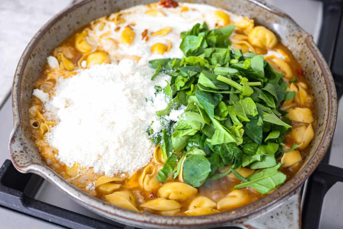 Get ready to impress with One-Pan Marry Me Tortellini! This 20-minute dish is made with cheese tortellini simmered in a rich sun-dried tomato cream sauce infused with garlic, fresh spinach, and parmesan. You'll fall in love with every bite! Close up shot of cheese, spinach and cream added to the tortellini and sauce.
