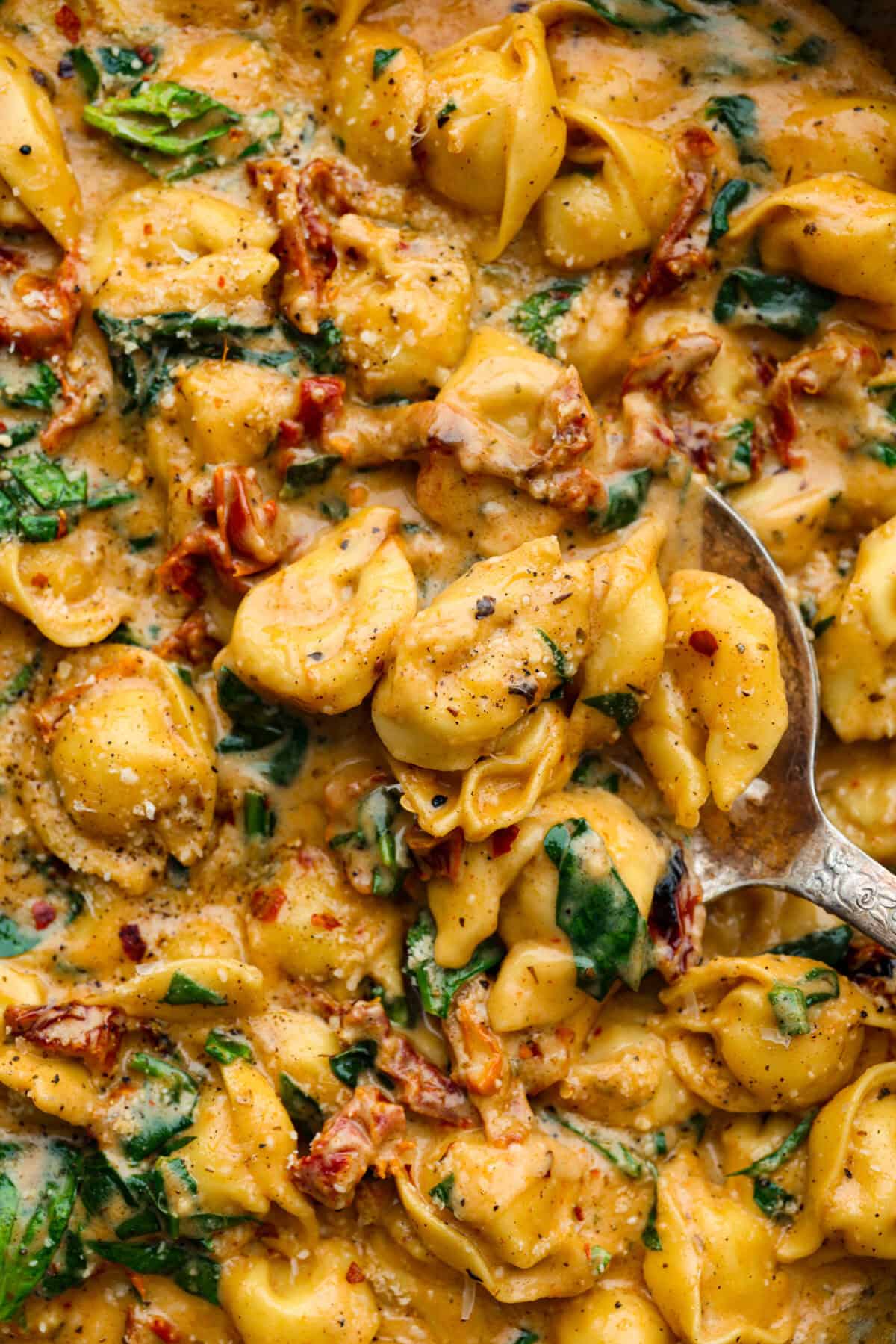 Get ready to impress with One-Pan Marry Me Tortellini! This 20-minute dish is made with cheese tortellini simmered in a rich sun-dried tomato cream sauce infused with garlic, fresh spinach, and parmesan. You'll fall in love with every bite! Close up shot of Marry Me tortellini.