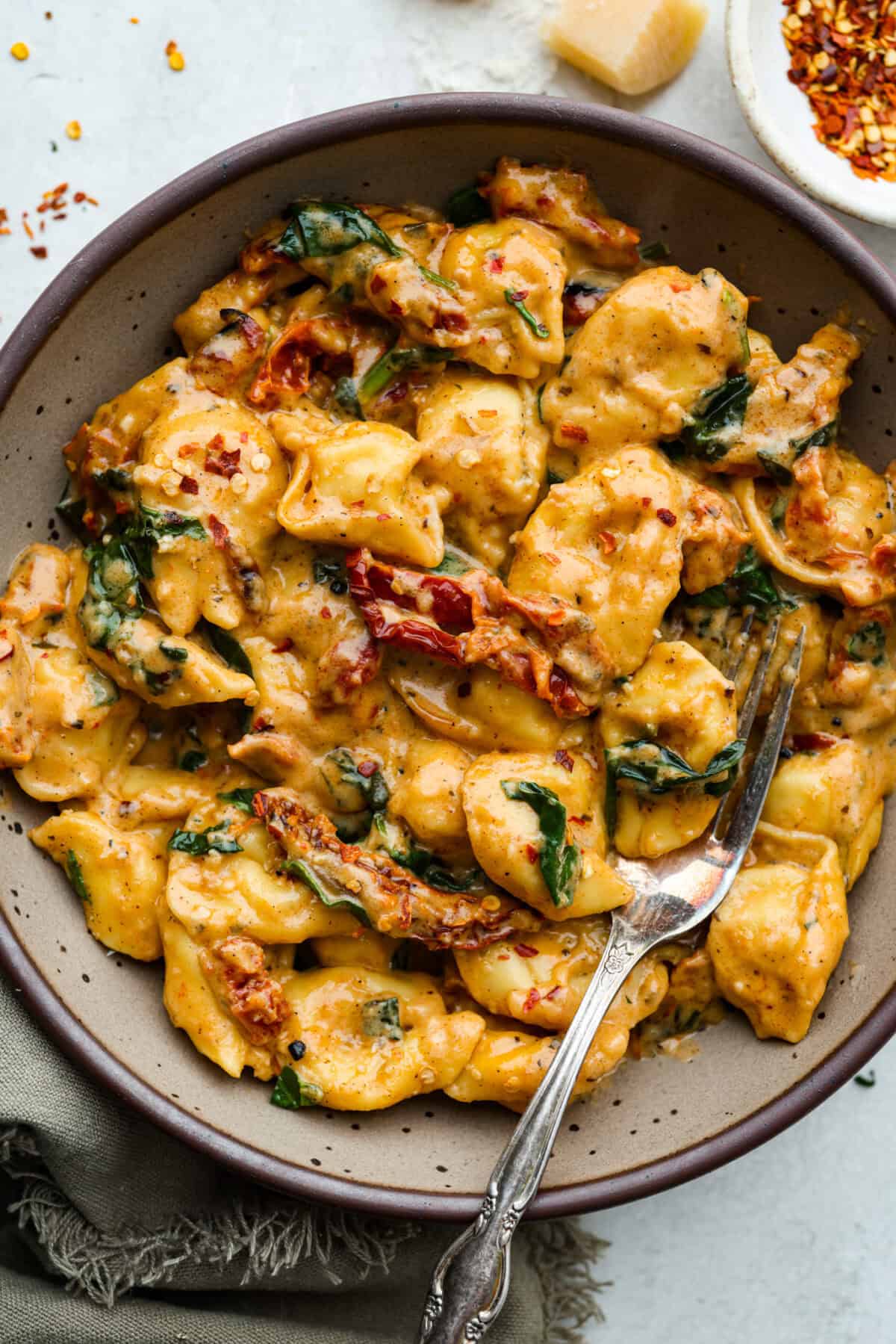 Get ready to impress with One-Pan Marry Me Tortellini! This 20-minute dish is made with cheese tortellini simmered in a rich sun-dried tomato cream sauce infused with garlic, fresh spinach, and parmesan. You'll fall in love with every bite! Overhead shot of Plated Marry Me tortellini.