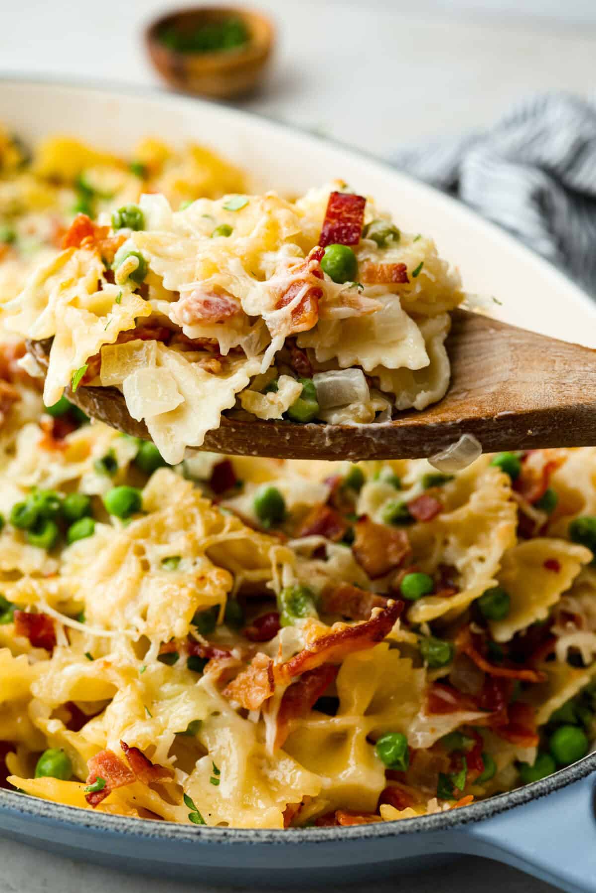 Stanley Tucci pasta casserole is everything you want in a casserole. It's simple to make and incredibly flavorful! TikTok is going crazy over the crispy bacon, tender peas, and the creamy, cheesy sauce that holds everything together! Close up shot of a scoop of Stanley Tucci pasta casserole on a wooden spoon.