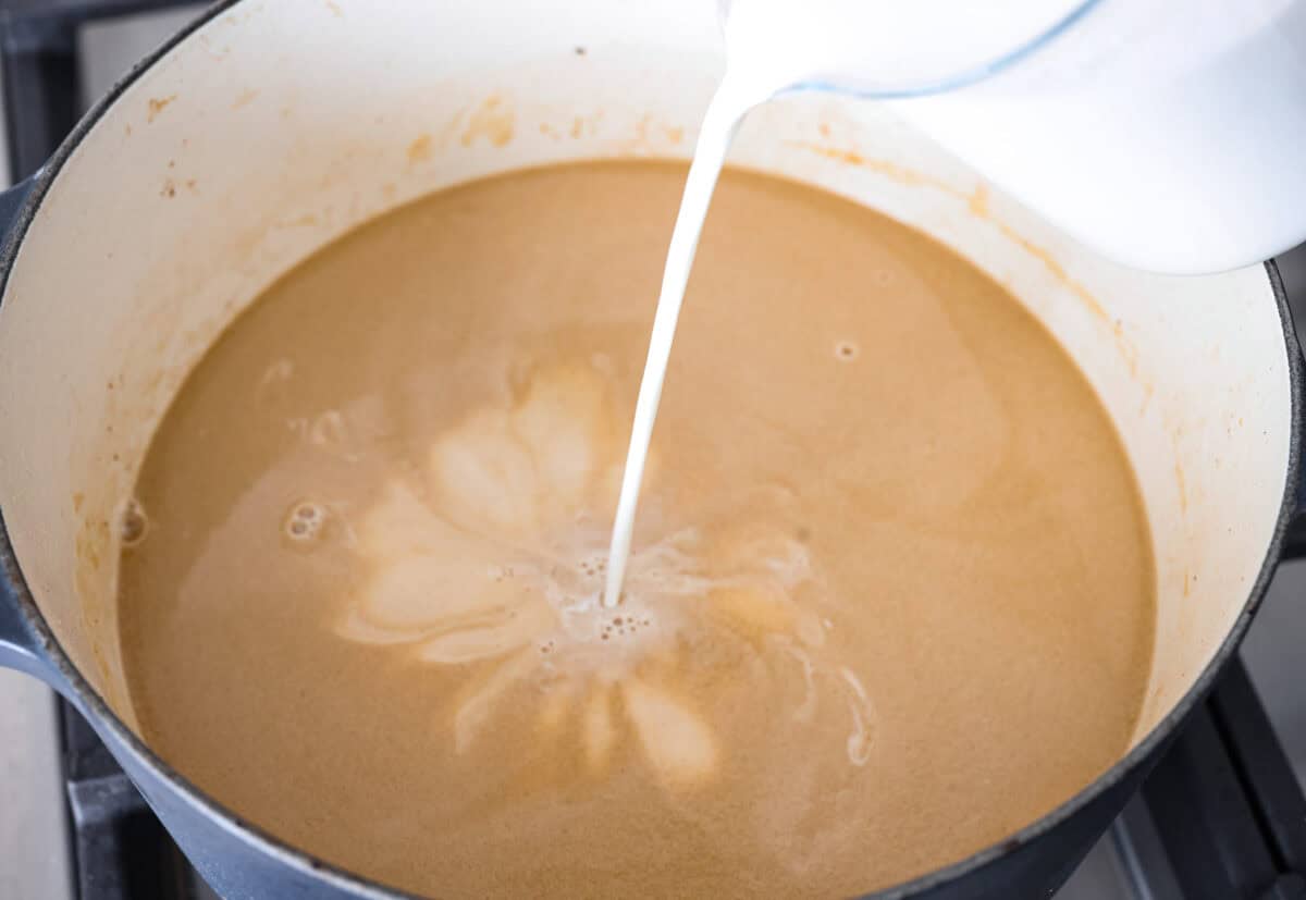 Warm and comforting, this cozy Swedish meatball soup is the perfect meal for chilly days. Juicy meatballs simmer in a rich, savory broth with tender noodles, making every spoonful satisfying. It’s easy to make and sure to become a family favorite! Angle shot of someone pouring half and half into the beef broth and onion mixture.