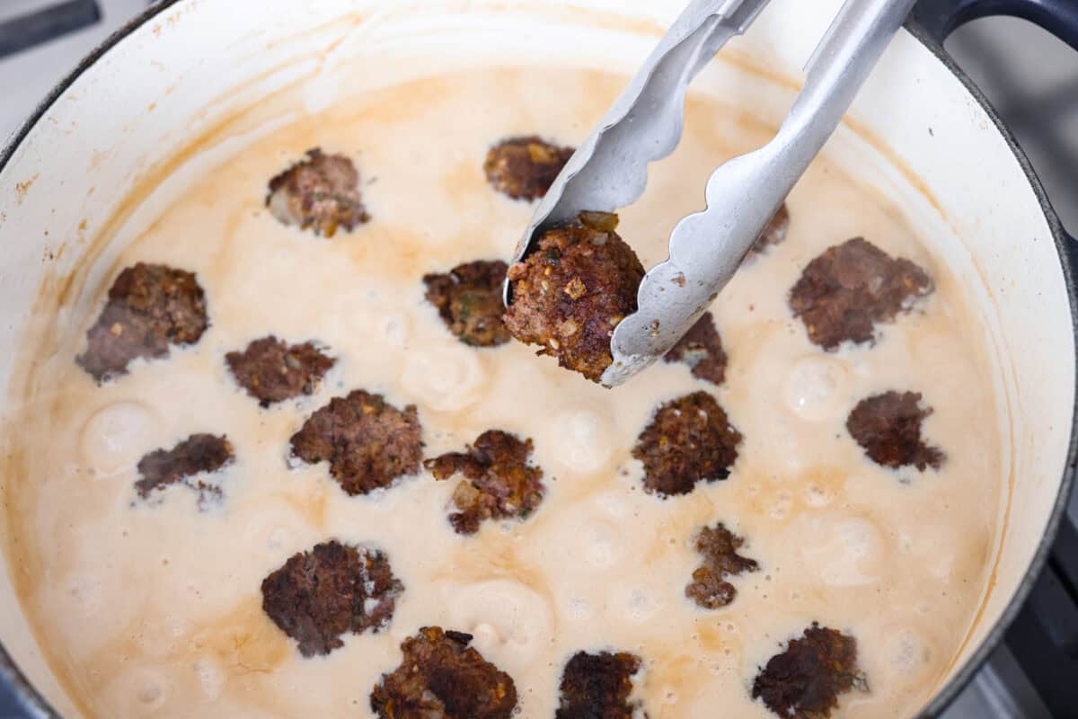 Warm and comforting, this cozy Swedish meatball soup is the perfect meal for chilly days. Juicy meatballs simmer in a rich, savory broth with tender noodles, making every spoonful satisfying. It’s easy to make and sure to become a family favorite! Overhead shot of someone placing the meatballs into the cream broth.