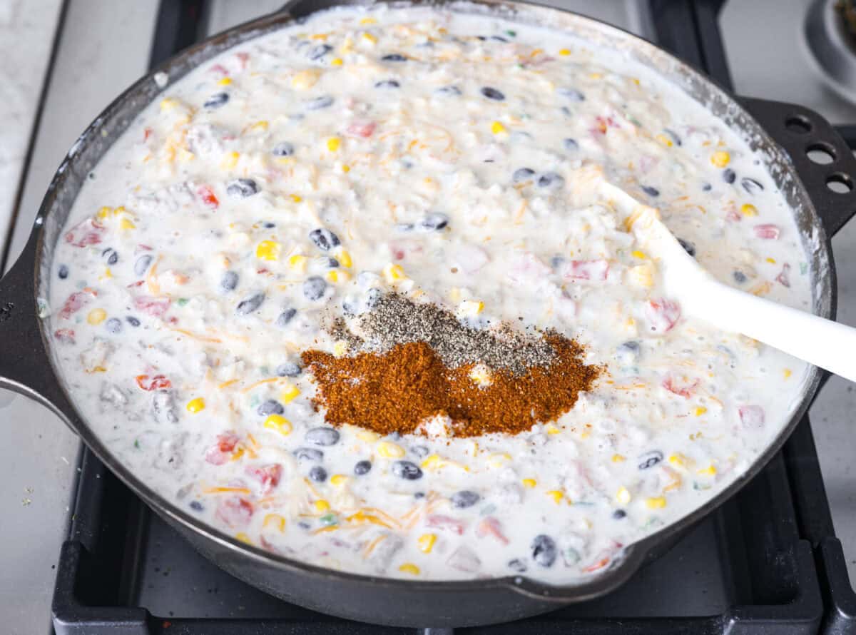 Creamy, cheesy Cowboy Mac and Cheese gets a bold twist with hearty additions like seasoned meat, tomatoes, jalapeรฑos, corn, beans, and onions. It's rich, flavorful, and just the right amount of spice! The heat is warm but not overwhelming. If you like it spicy, add more jalapeรฑos! Overhead shot of the cheese, chili powder and salt and pepper added to the mixture.