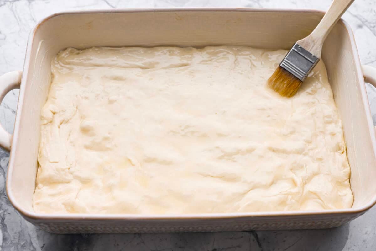 Pizza Hut breadsticks are warm, fluffy, and buttery, but this copycat recipe is even better! Coated in seasoning, parmesan, and melted butter, theyโre next-level delicious. Someone brushing melted butter over the dough in a 9x13 baking dish.