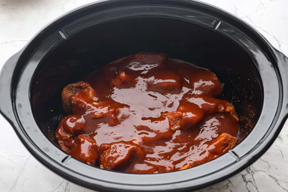 My slow cooker boneless pork ribs (or country style ribs) are unbelievably tender and loaded with tangy BBQ flavor! They cook low and slow all day, resulting in juicy, fork tender perfection with minimal effort. Overhead shot of ribs covered in bbq sauce in a slow cooker.