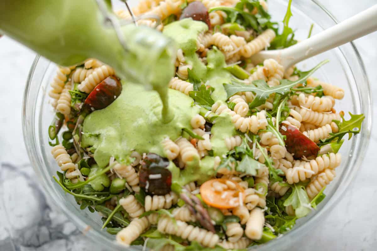 This Green Goddess Pasta Salad is fresh, vibrant, and full of flavor! The creamy herb dressing adds a tangy twist, while crisp spring veggies make it light yet hearty. Perfect for potlucks or any time youโre craving a delicious side! Process shot of someone pouring the dressing over the combined salad ingredients.