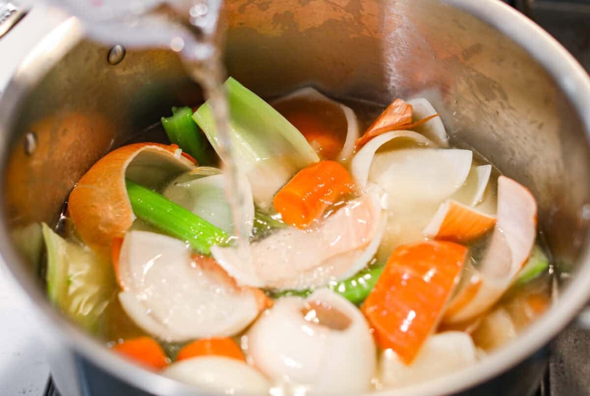 Homemade vegetable broth is light, delicate, and infused with the flavor of fresh vegetables. It's incredibly easy to make and great for using leftover veggies. The key is to not overcook the veggies. This can lead to a bitter flavored broth. Someone pouring water over the veggies in a pot.