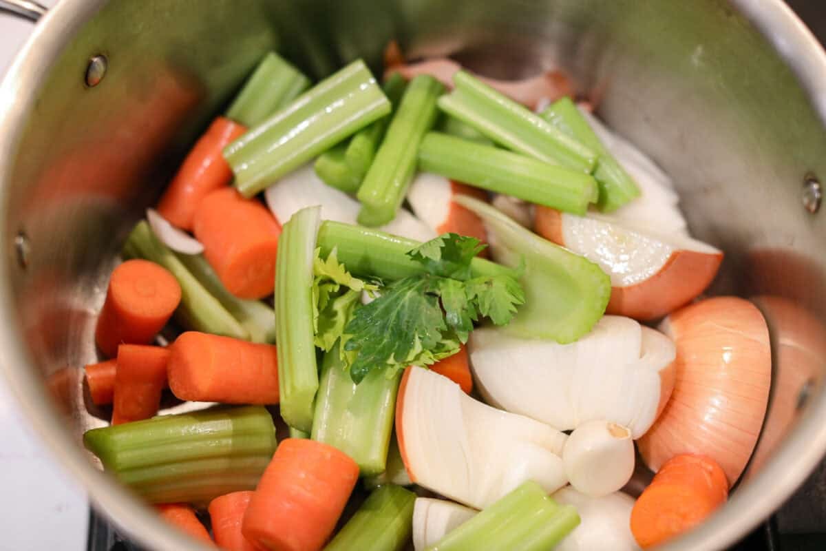Homemade vegetable broth is light, delicate, and infused with the flavor of fresh vegetables. It's incredibly easy to make and great for using leftover veggies. The key is to not overcook the veggies. This can lead to a bitter flavored broth. Close up shot of a pile of veggies in a stock pot.