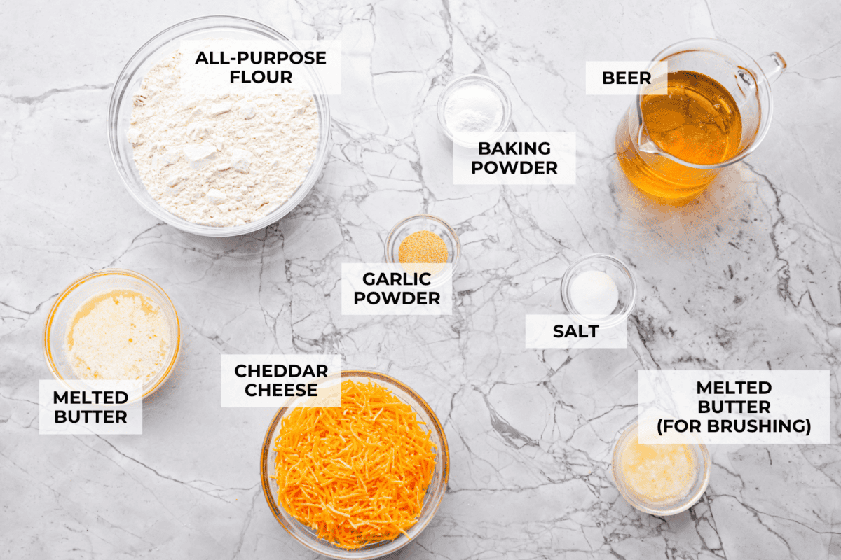 These cheesy beer bread muffins are light, fluffy, and packed with savory flavor! The key is to not overmix the batter. Mixing until just combined will give you the perfect airy, melt-in-your-mouth texture that will keep you coming back for more. Overhead shot of labeled ingredients.