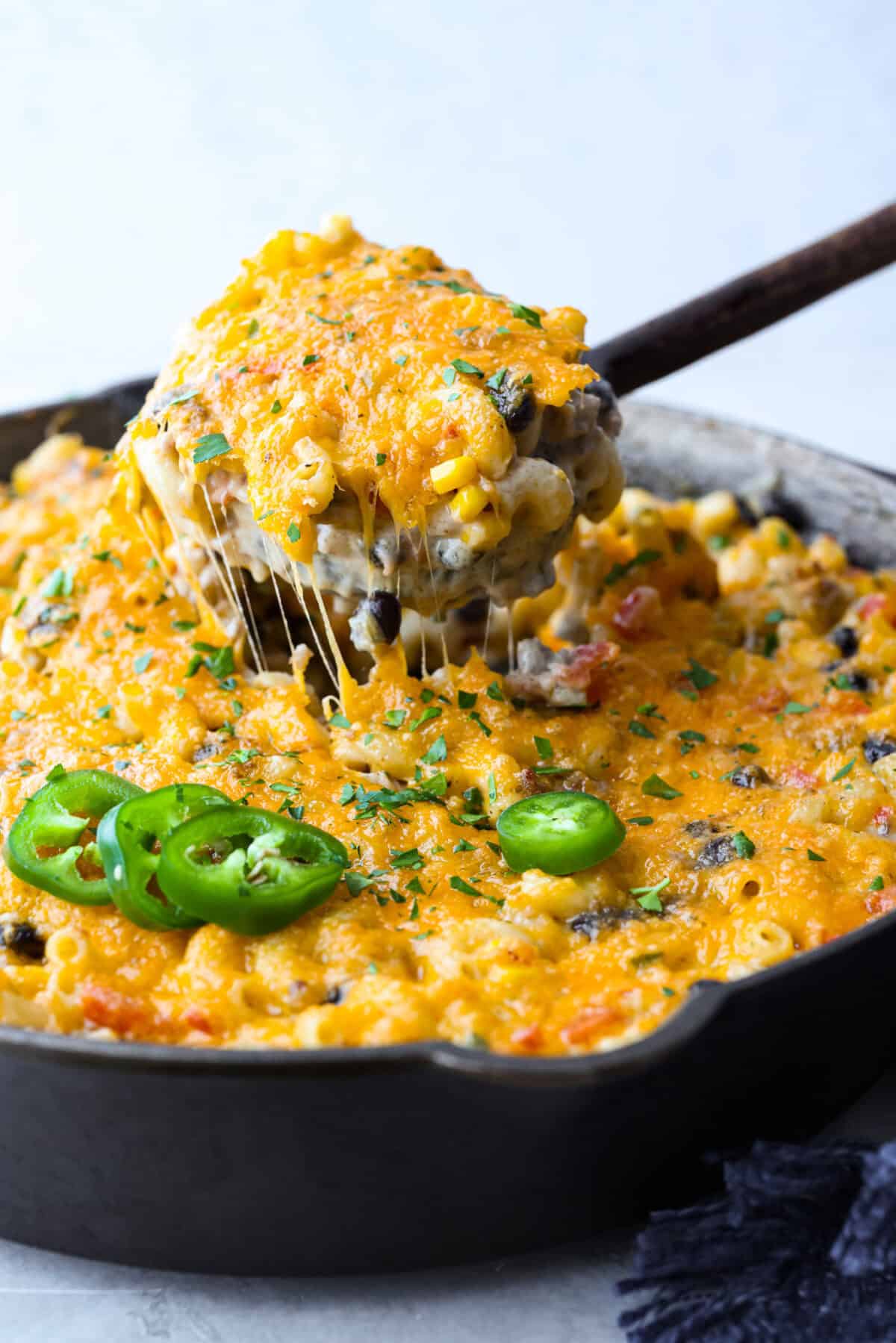 Creamy, cheesy Cowboy Mac and Cheese gets a bold twist with hearty additions like seasoned meat, tomatoes, jalapeรฑos, corn, beans, and onions. It's rich, flavorful, and just the right amount of spice! The heat is warm but not overwhelming. If you like it spicy, add more jalapeรฑos! Close up shot of someone pulling a scoop of cowboy mac and cheese out of the skillet.