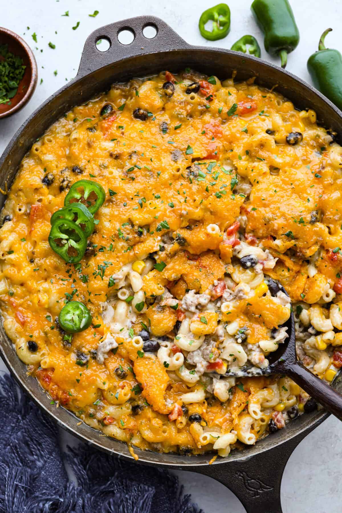 Creamy, cheesy Cowboy Mac and Cheese gets a bold twist with hearty additions like seasoned meat, tomatoes, jalapeรฑos, corn, beans, and onions. It's rich, flavorful, and just the right amount of spice! The heat is warm but not overwhelming. If you like it spicy, add more jalapeรฑos! Tops down shot of cowboy mac and cheese in a skillet, garnished with sliced jalapeรฑo.