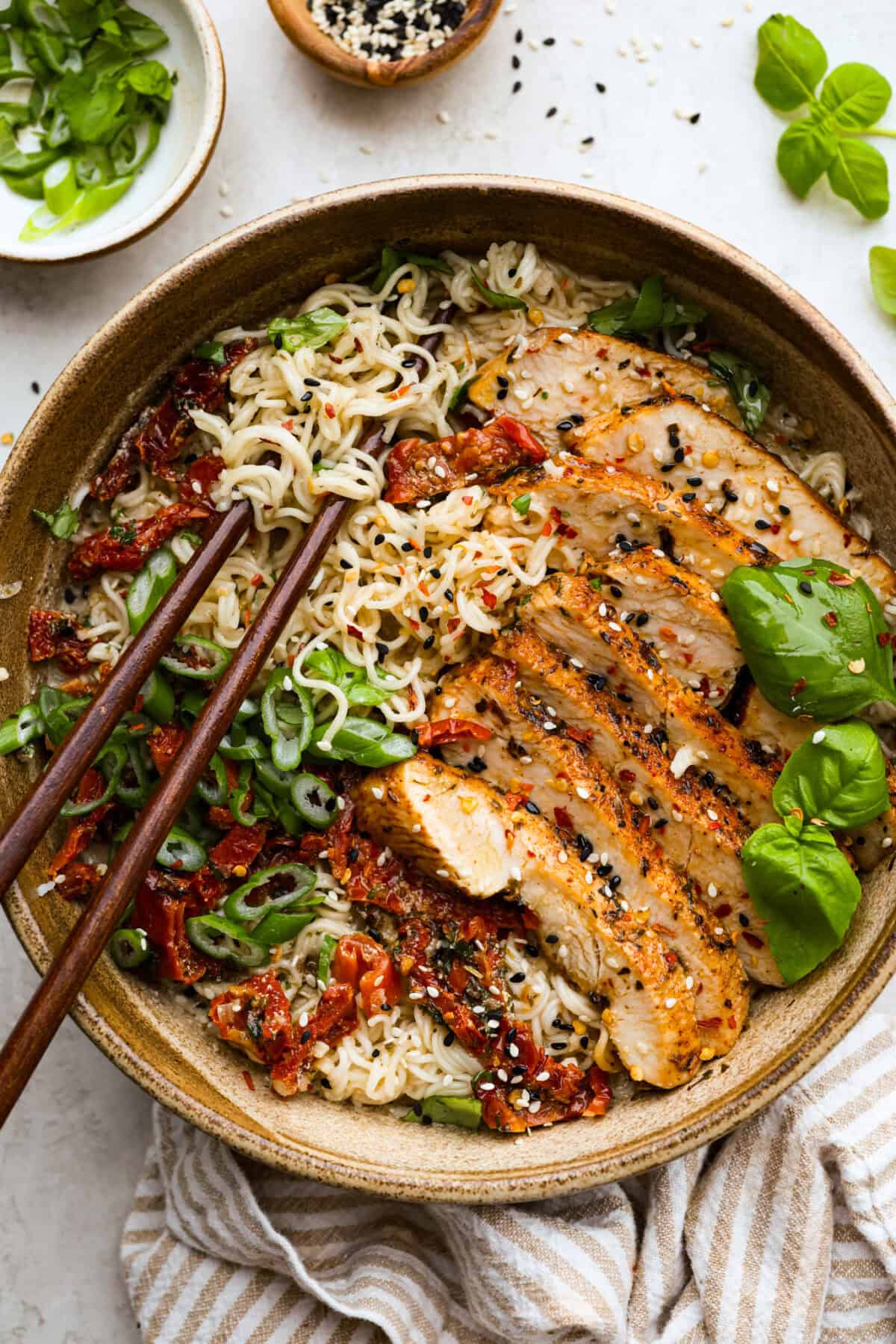 A top-down view of Marry Me Ramen with grilled chicken, sun-dried tomatoes, green onions, sesame seeds, and fresh basil. A comforting and creamy ramen dish full of bold flavors.