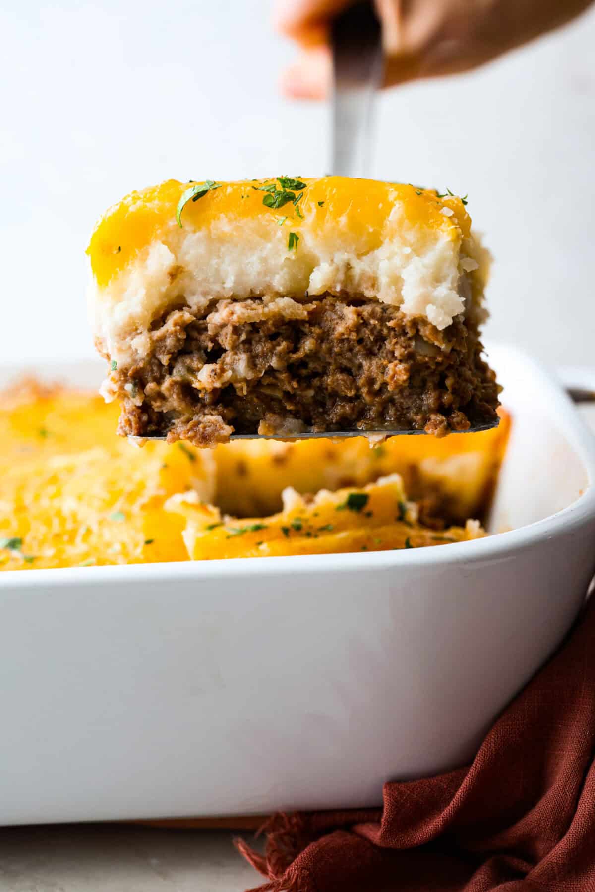 Turn classic meatloaf into amazing one-pan Meatloaf Casserole! Juicy, flavorful meatloaf and creamy mashed potatoes come together in one easy, delicious dish. Side shot of someone lifting a serving of meatloaf casserole out of the baking dish.