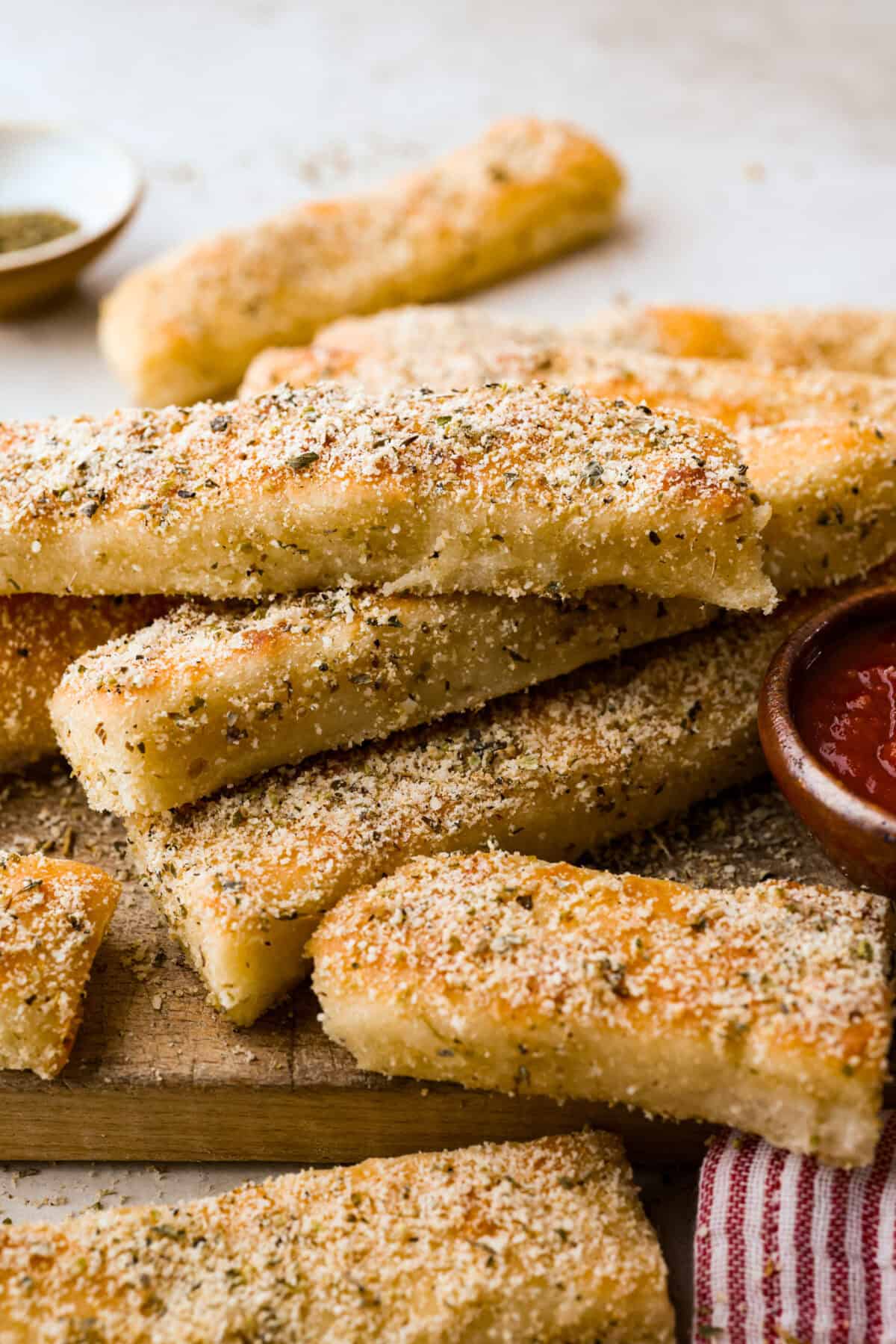 Pizza Hut breadsticks are warm, fluffy, and buttery, but this copycat recipe is even better! Coated in seasoning, parmesan, and melted butter, theyโre next-level delicious. Pile of Pizza Hut breadsticks on a cutting board with a bowl of marinara sauce next to them.