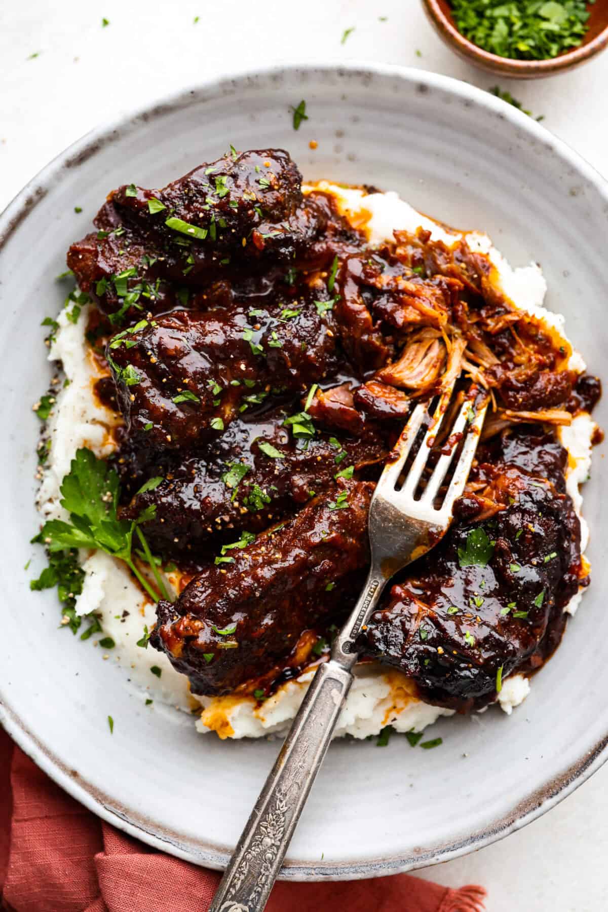 My slow cooker boneless pork ribs (or country style ribs) are unbelievably tender and loaded with tangy BBQ flavor! They cook low and slow all day, resulting in juicy, fork tender perfection with minimal effort. Overhead shot of plated slow cooker boneless pork ribs over mashed potatoes.