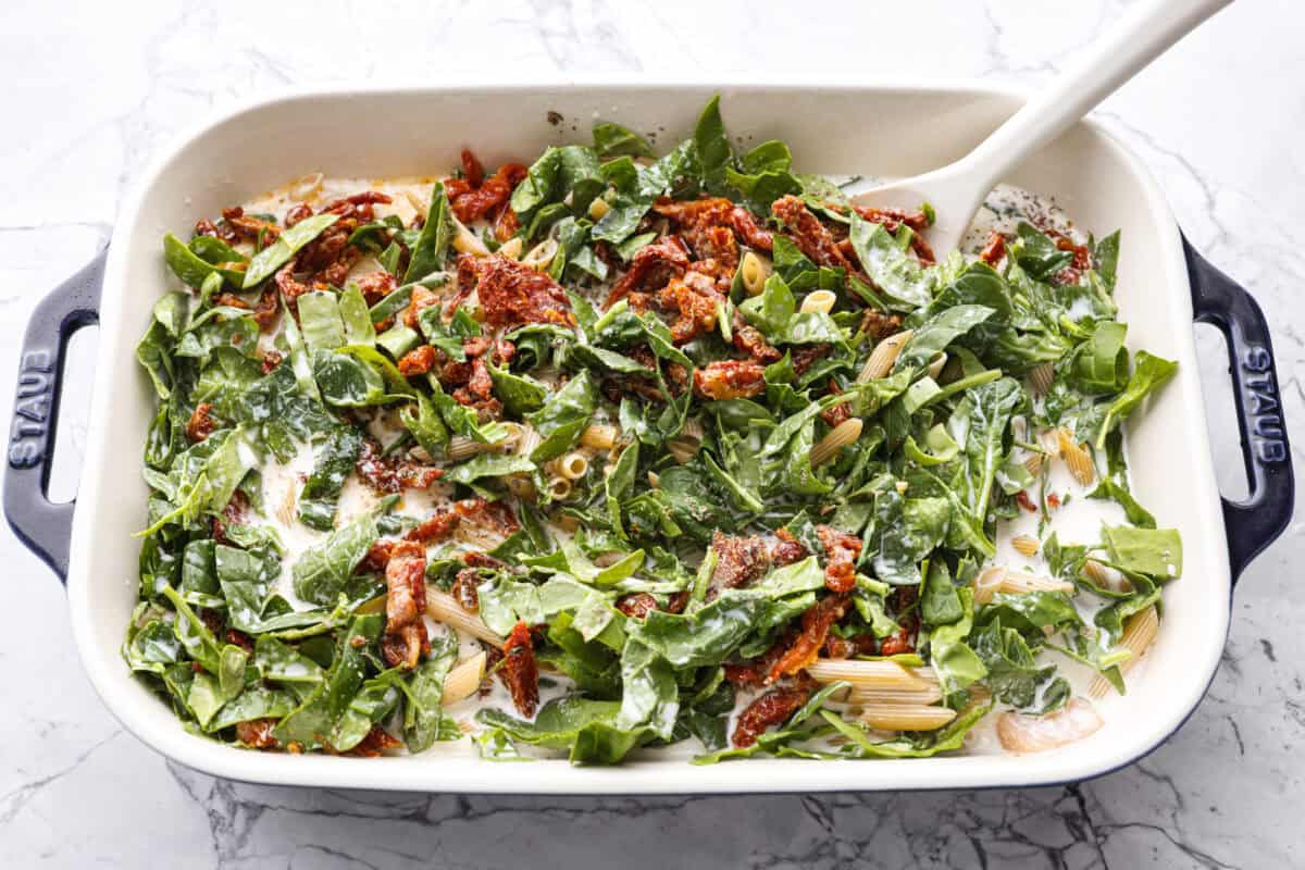You all love my Crockpot Tuscan Chicken, and I know casseroles are a favorite as well. So, I combined them into this irresistibly delicious Tuscan Chicken Casserole! Someone stirring all of the ingredients in the baking dish.