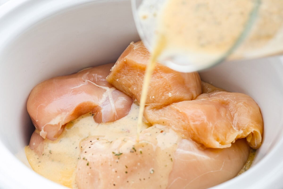 You guys can't get enough of my 3 packet roast, so it's time for a new version, 3 Packet Crockpot Chicken! It takes just 5 minutes to prep and comes out juicy, tender, and full of flavor. Someone pouring mixture over the chicken in the crockpot.