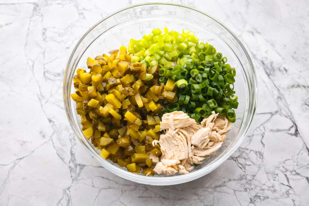 If you love that good pickle crunch, this high-protein Dill Pickle Chicken Salad is a must! It’s bold, zesty, and perfect for sandwiches or a snack right out of the bowl! Bowl of pickles, chicken, onion and celery.