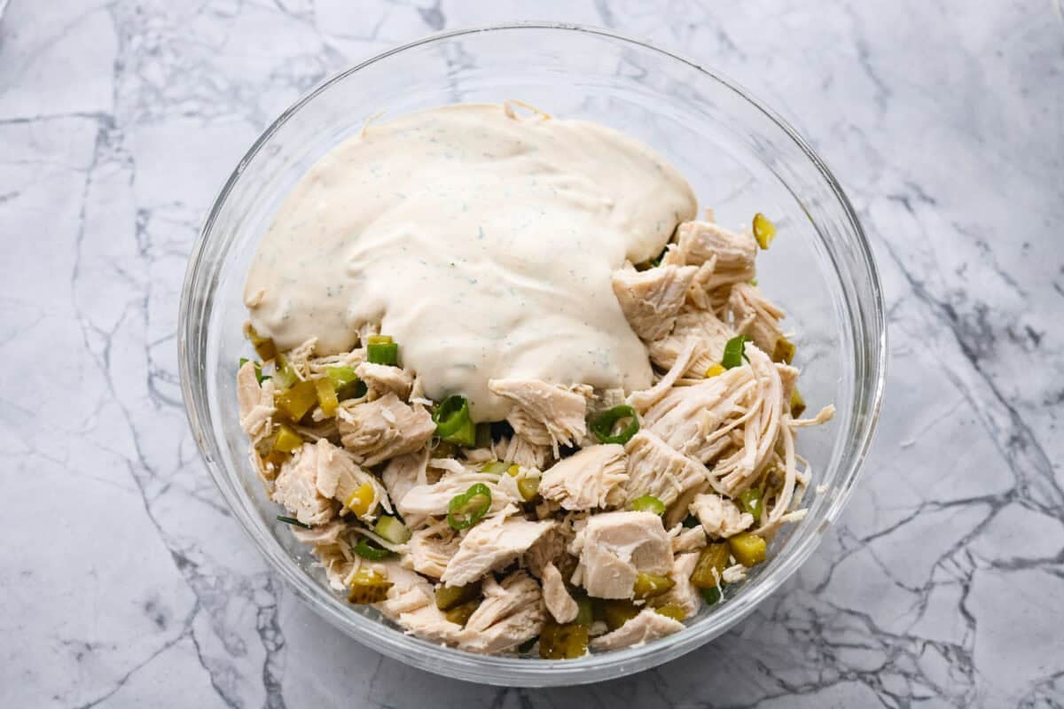 If you love that good pickle crunch, this high-protein Dill Pickle Chicken Salad is a must! It’s bold, zesty, and perfect for sandwiches or a snack right out of the bowl! Mixed dressing poured over the chicken mixture in a bowl.