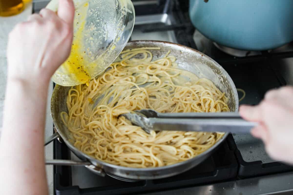 You guys! My pasta carbonara is the real deal—creamy, dreamy, and so full of flavor! Just eggs, cheese, pancetta, and pasta magic. It feels restaurant worthy but takes less than 30 minutes! Someone pouring the carbonara sauce over the noodles in a skillet.