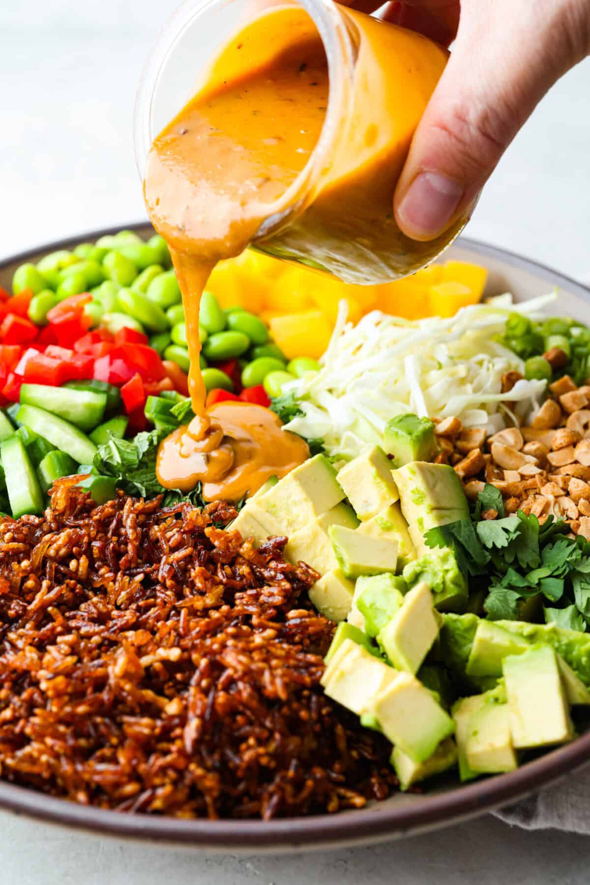 This trendy Crispy rice salad is a perfect mix of crunch, freshness, and bold flavor! Golden rice, vibrant veggies, and a creamy dressing make every bite irresistible. Someone drizzling the dressing over the crispy rice salad.