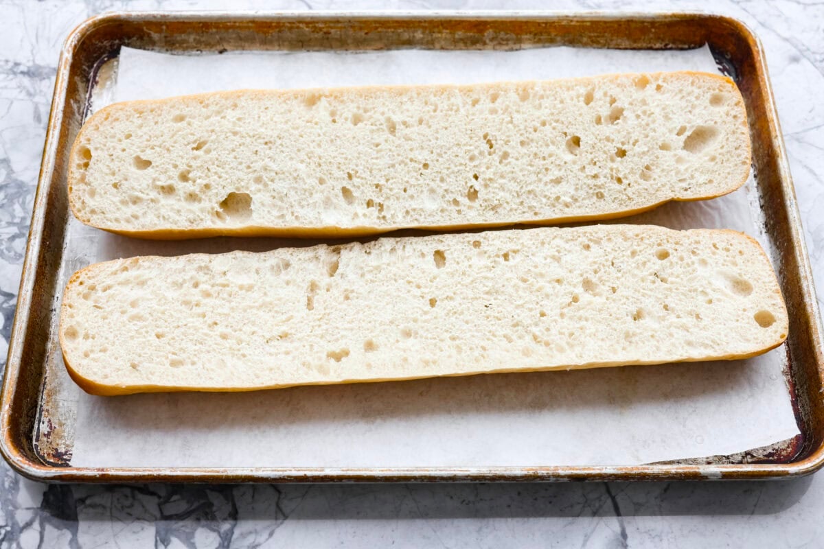 Iโm not saying Iโve eaten half a loaf of this Garlic Bread straight off the baking sheetโฆbut Iโm also not not saying that. Itโs golden, cheesy, dripping with garlicky butter, and so good! French bread cut in half and laying on parchment paper on a baking sheet.