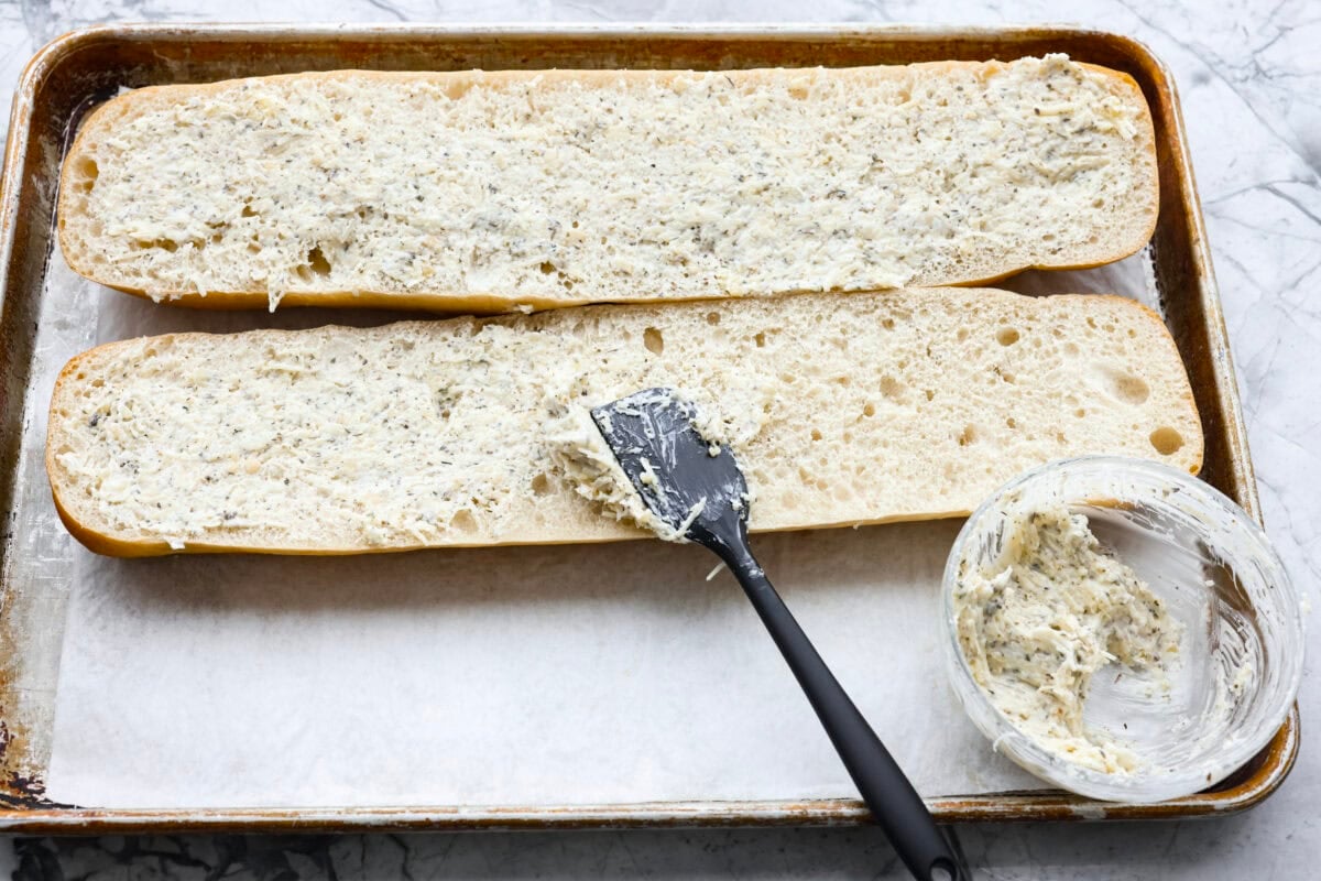 Iโm not saying Iโve eaten half a loaf of this Garlic Bread straight off the baking sheetโฆbut Iโm also not not saying that. Itโs golden, cheesy, dripping with garlicky butter, and so good! Someone spreading garlic butter on the French bread.